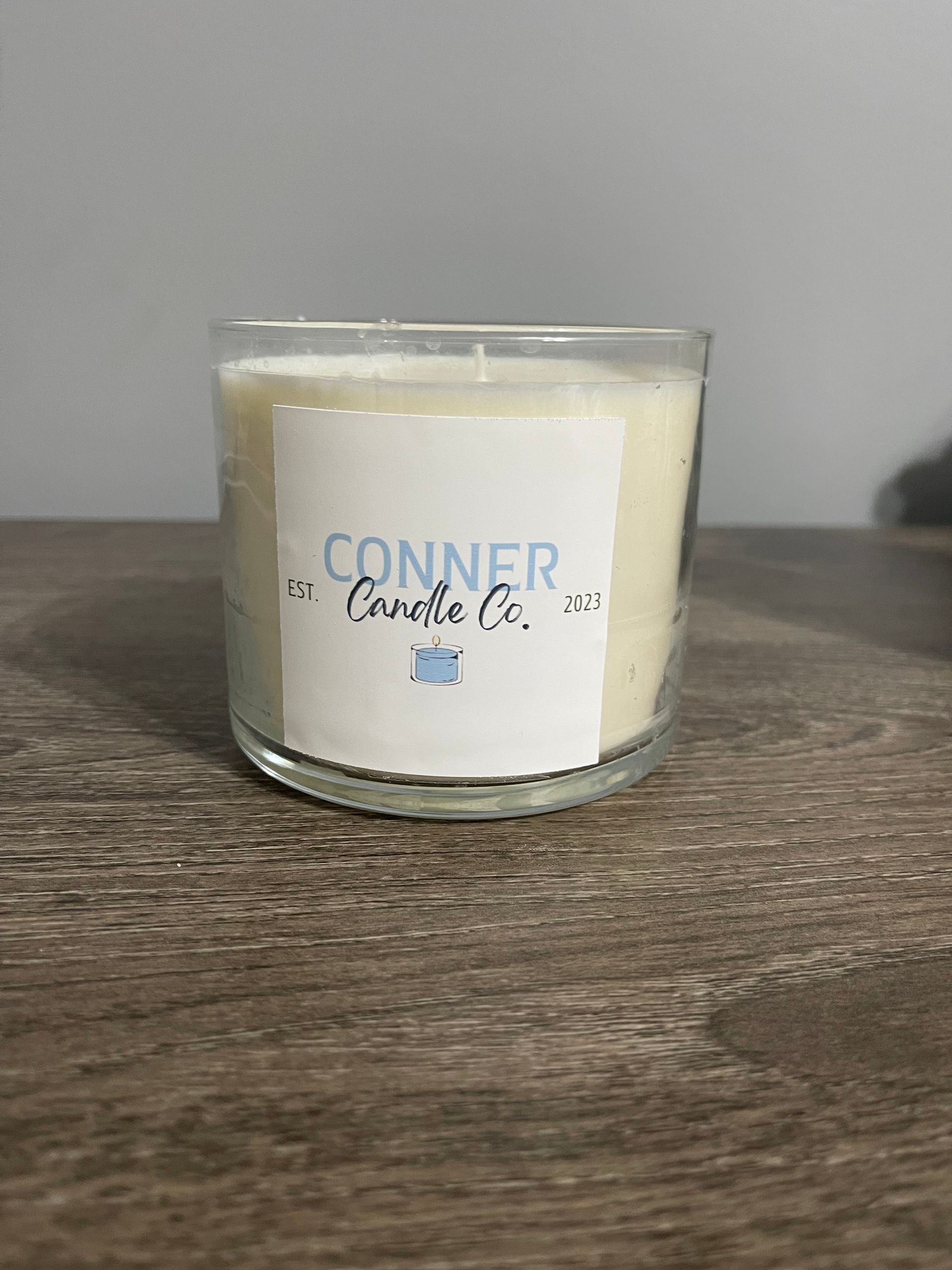 Candle in a clear glass container with a white label that says 