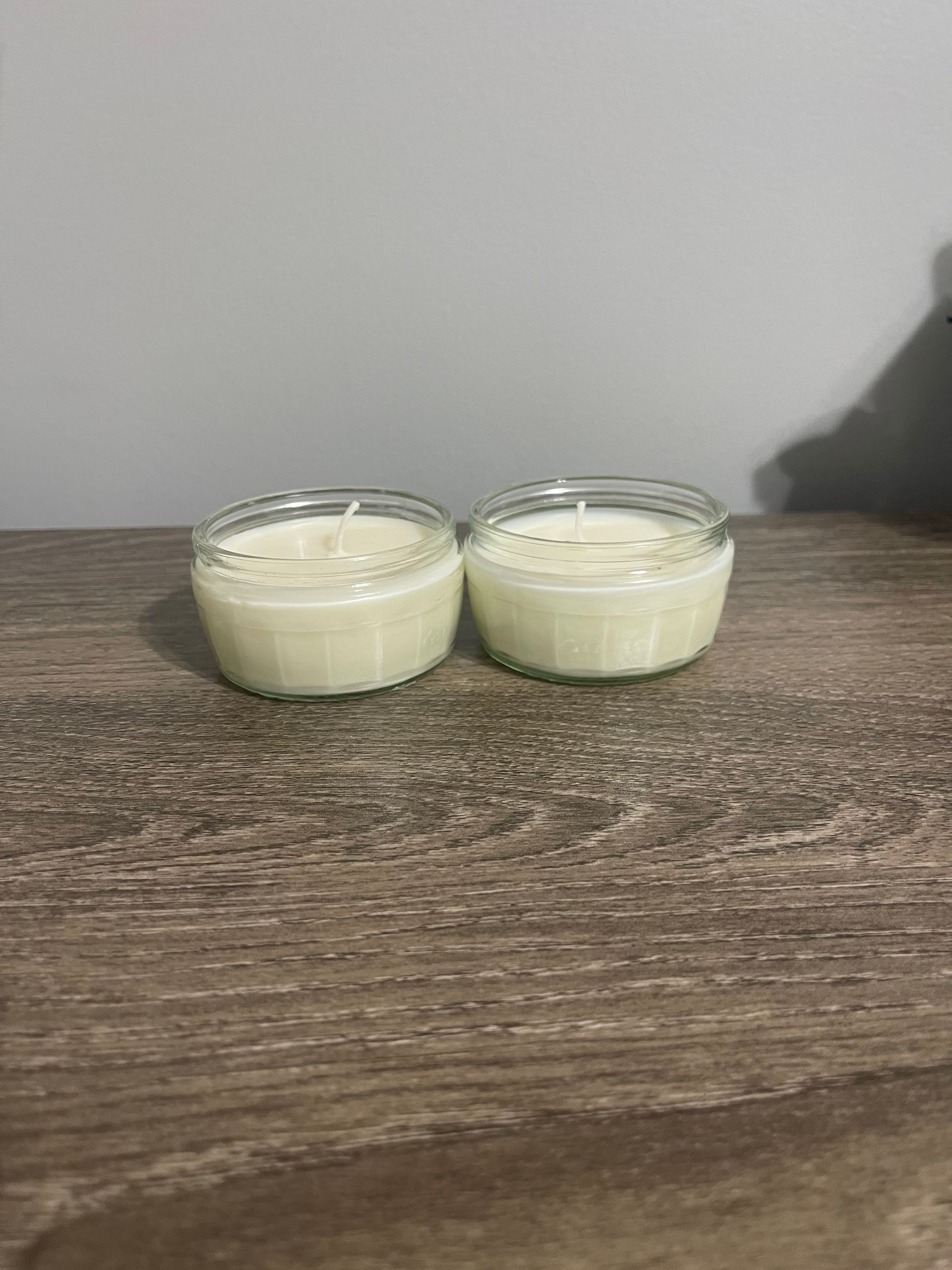 Two small, round, glass jar candles with white wax on a wood surface.