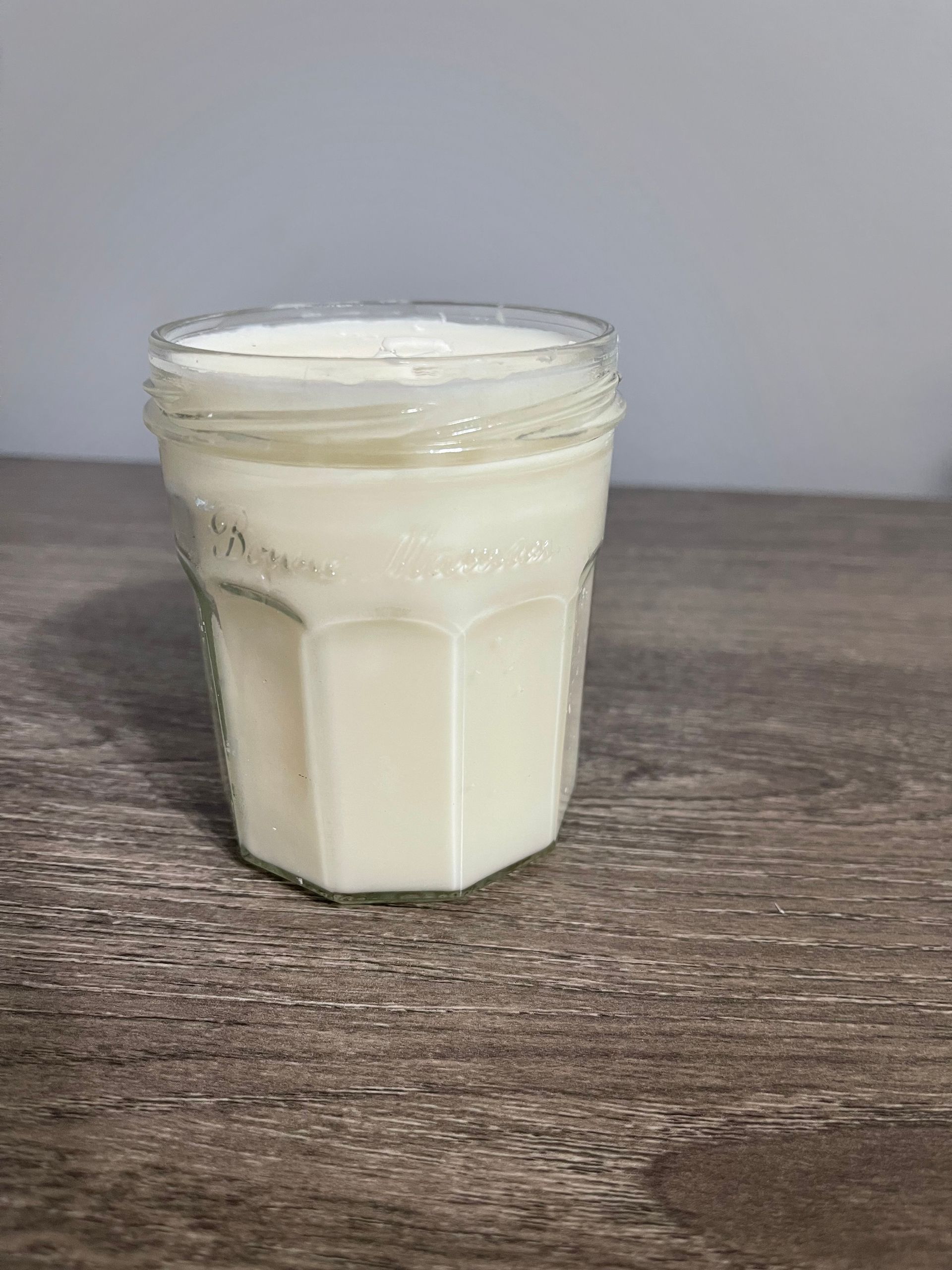A glass jar filled with a white, opaque liquid on a wood surface.