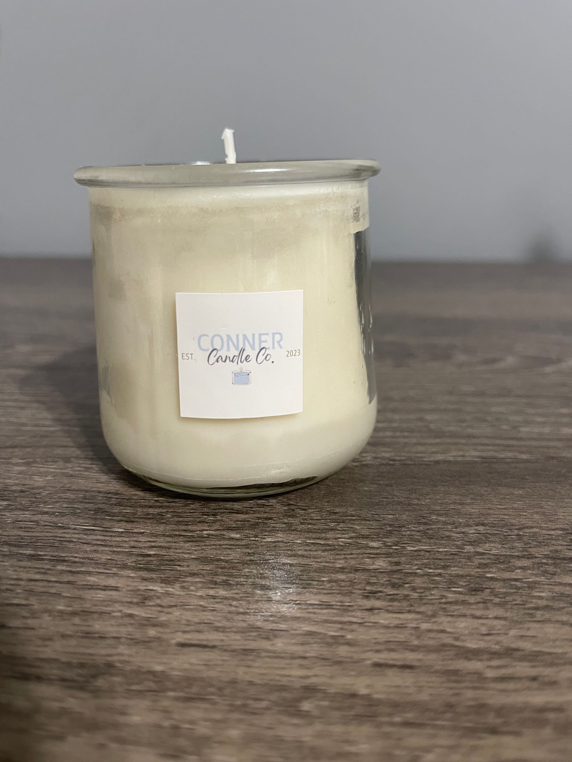 Cream-colored candle in a clear glass jar with a white label on a wooden surface.