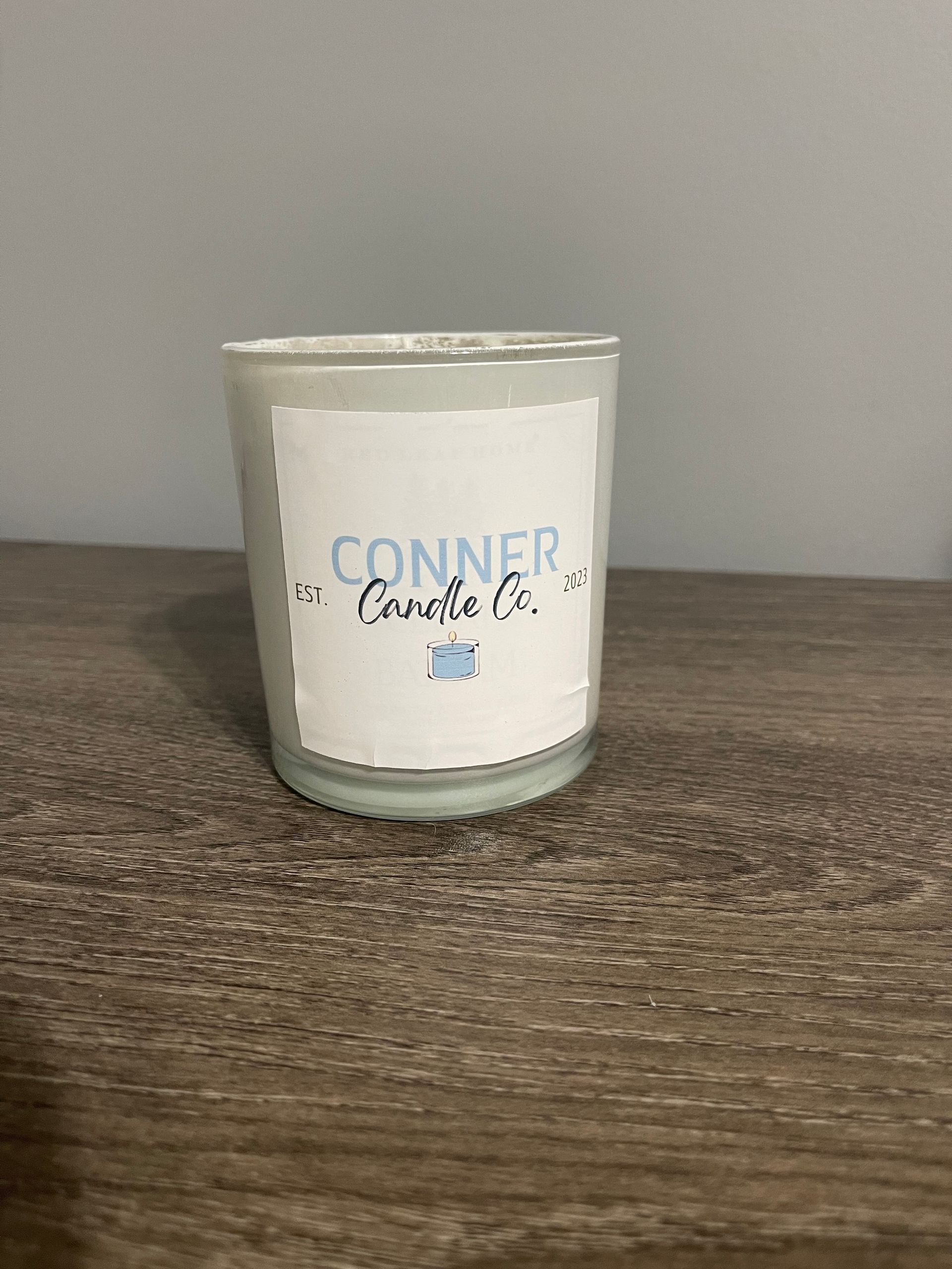 Conner Candle Co. candle in a clear glass jar with a blue and white label on a wooden surface.