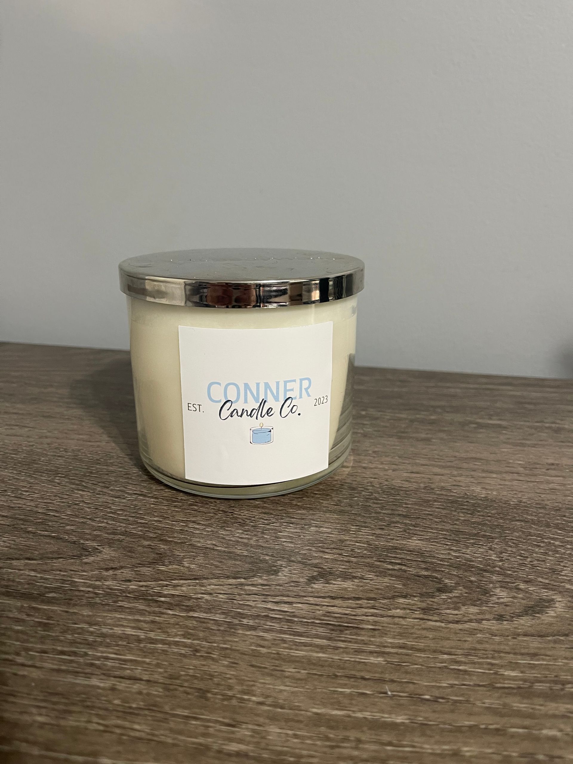 Candle in a glass jar with silver lid, labeled 