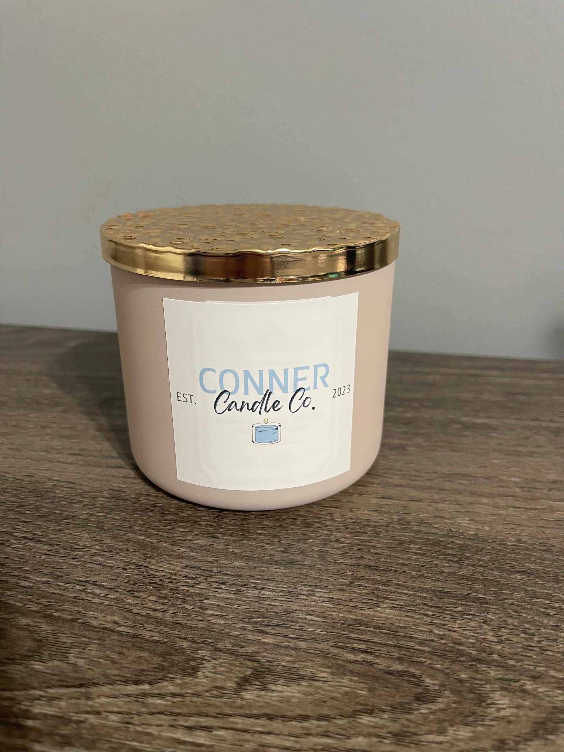 Pink candle in a jar with a gold lid, labeled 