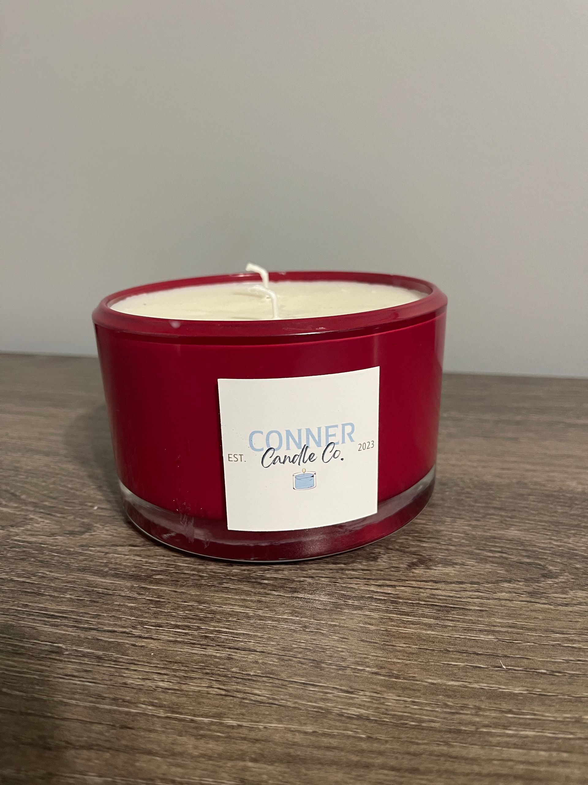 Red candle in a glass container with a white label.