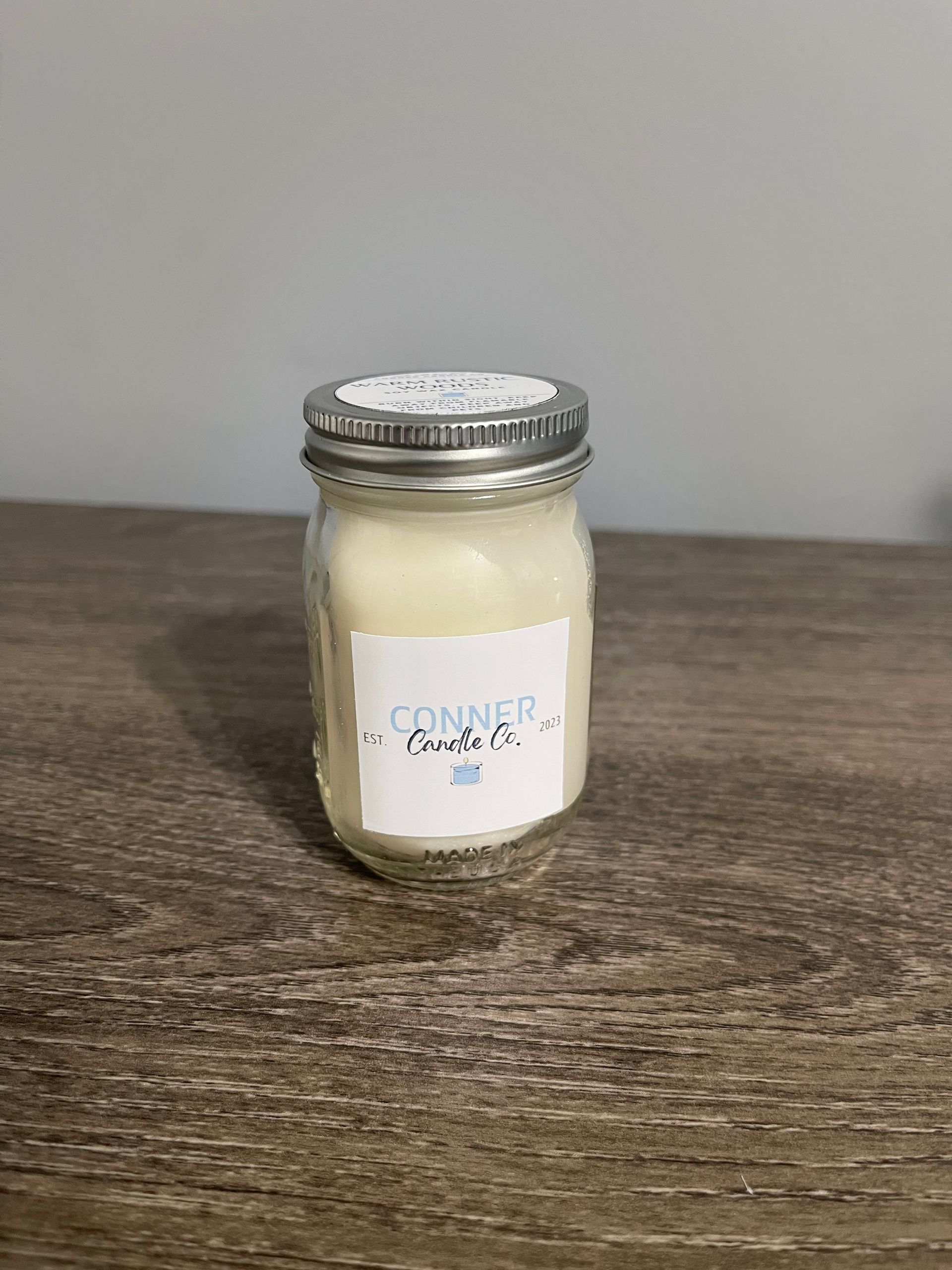 Candle in a jar with label on wooden surface.