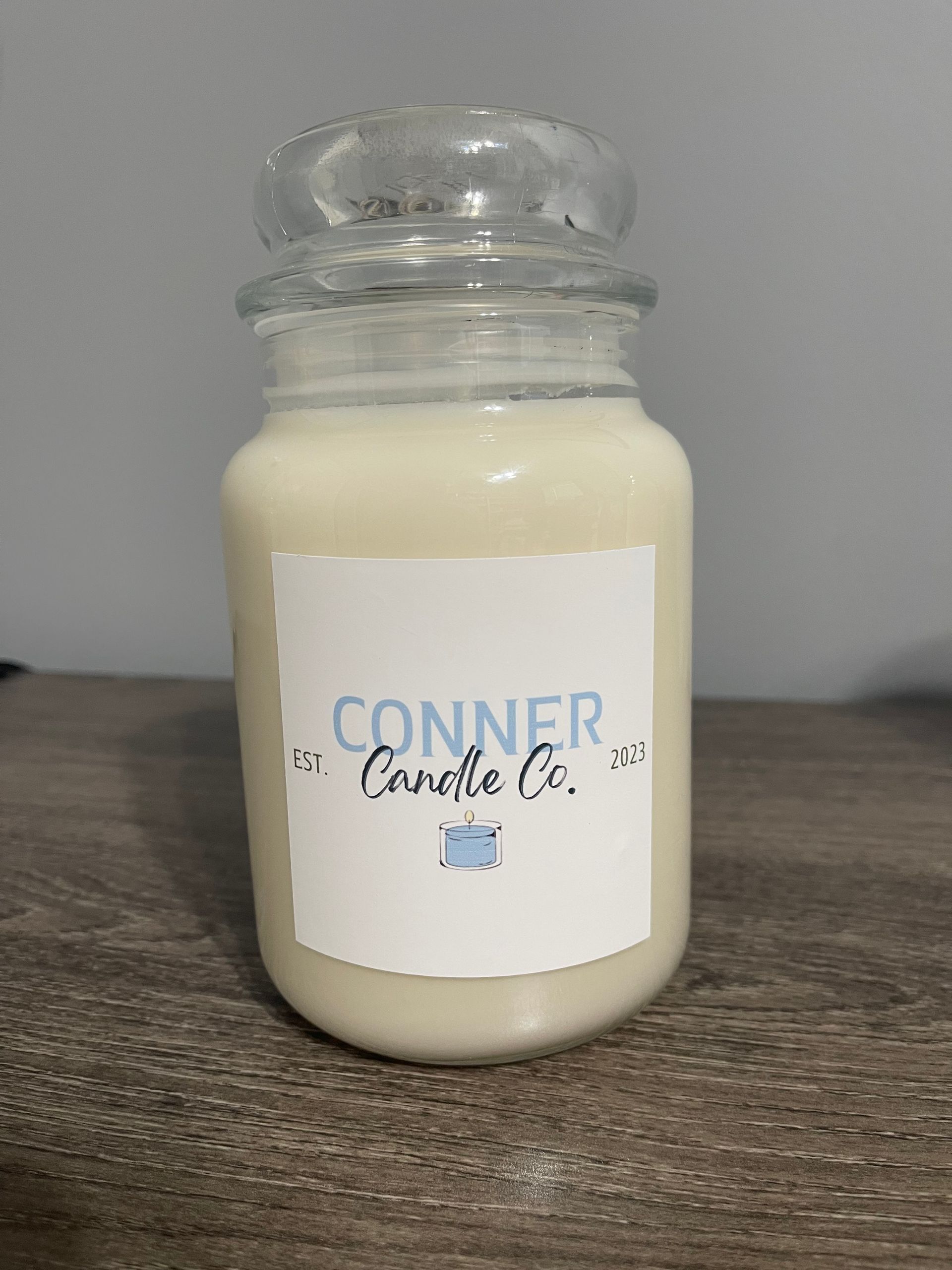 Three Conner Candle Co. candles in glass jars with lids, labeled on a wood surface.