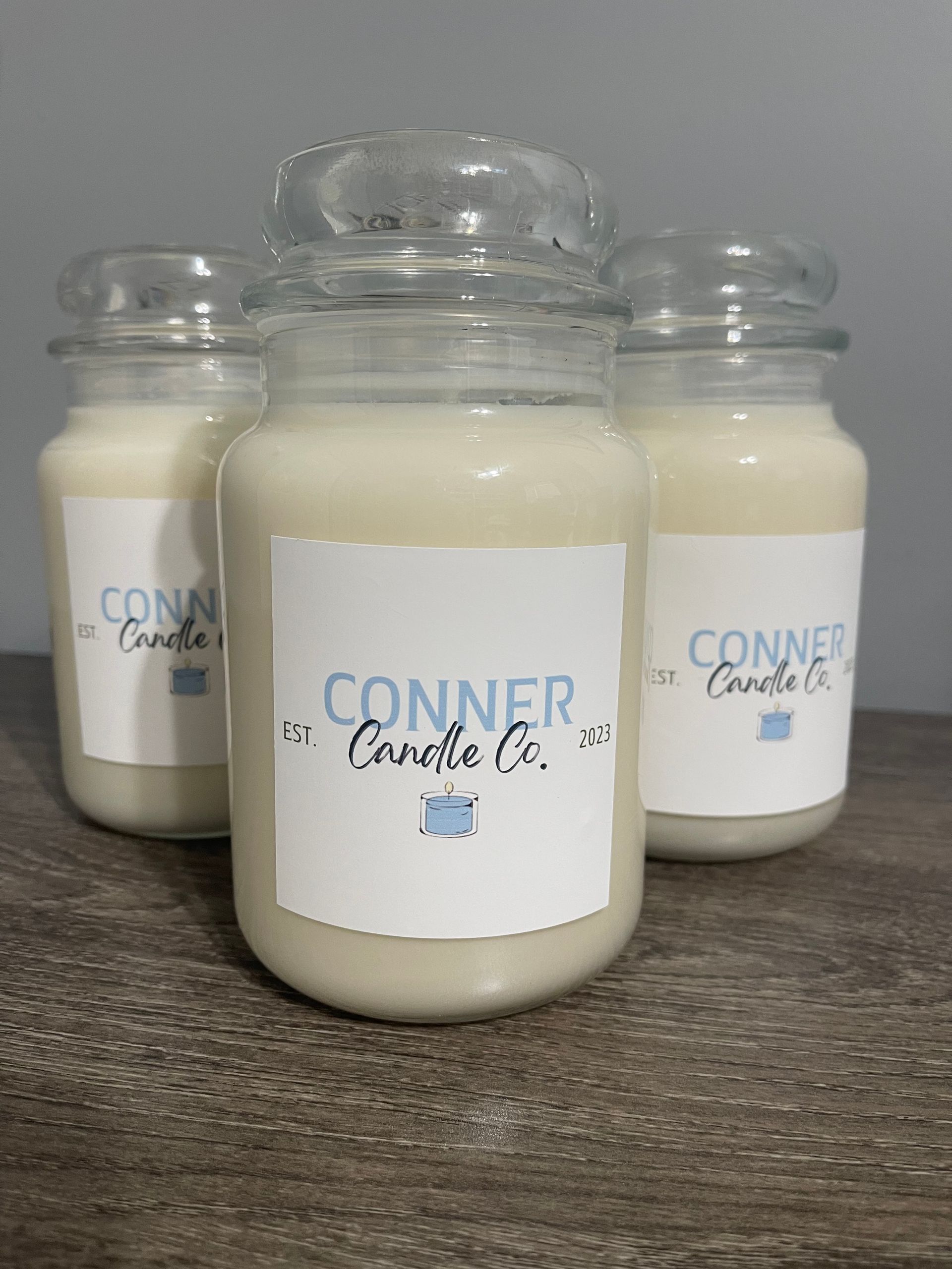 Three Conner Candle Co. candles in glass jars with lids, labeled on a wood surface.