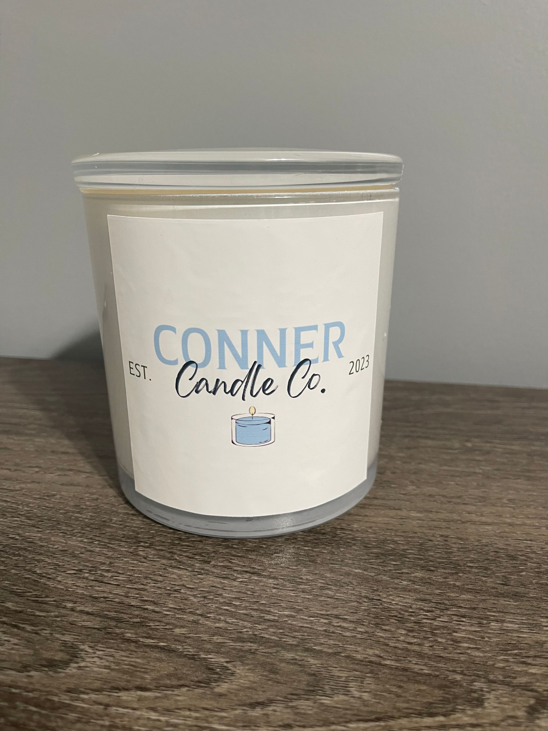 Conner Candle Co. candle in a clear glass container with a white label and a clear lid, sitting on a wooden surface.