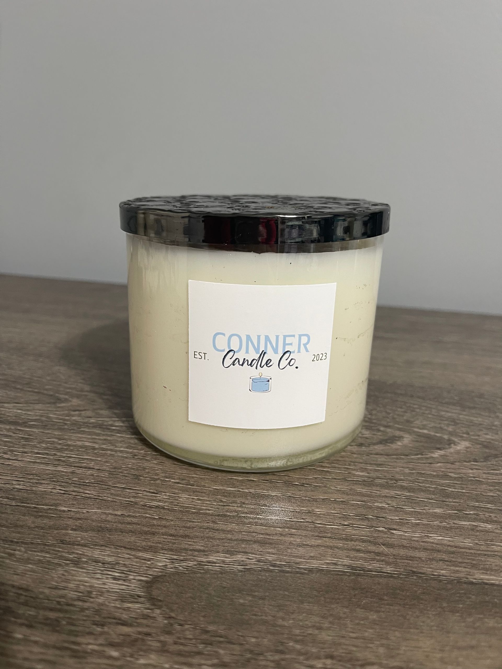 Cream-colored candle in a glass jar with a black lid and white label that says 
