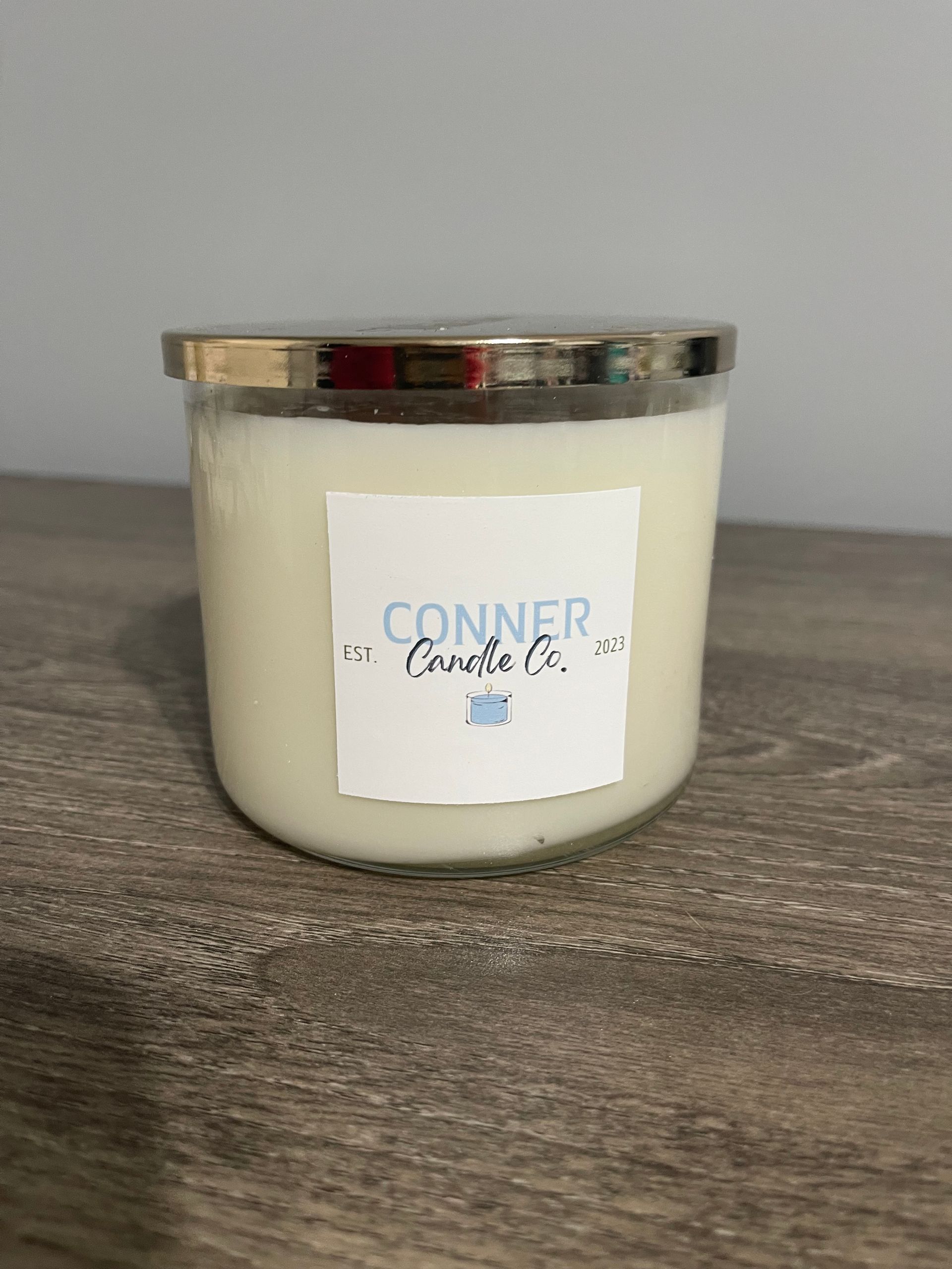 White candle in a glass jar with a gold lid, labeled 