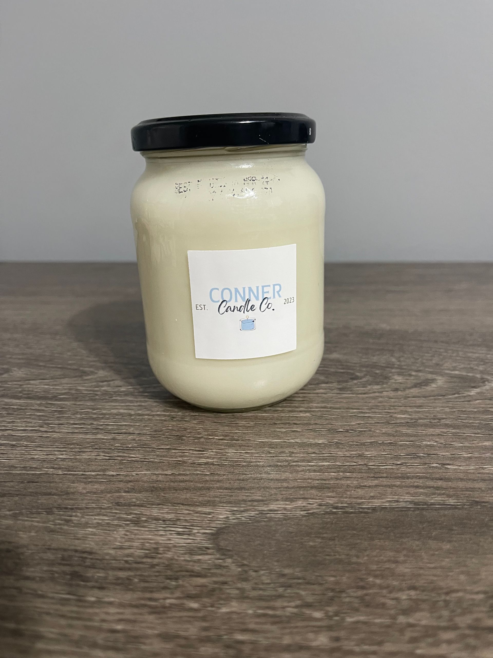 A jar with a black lid and a white label, filled with a light-colored substance, sits on a wooden surface.