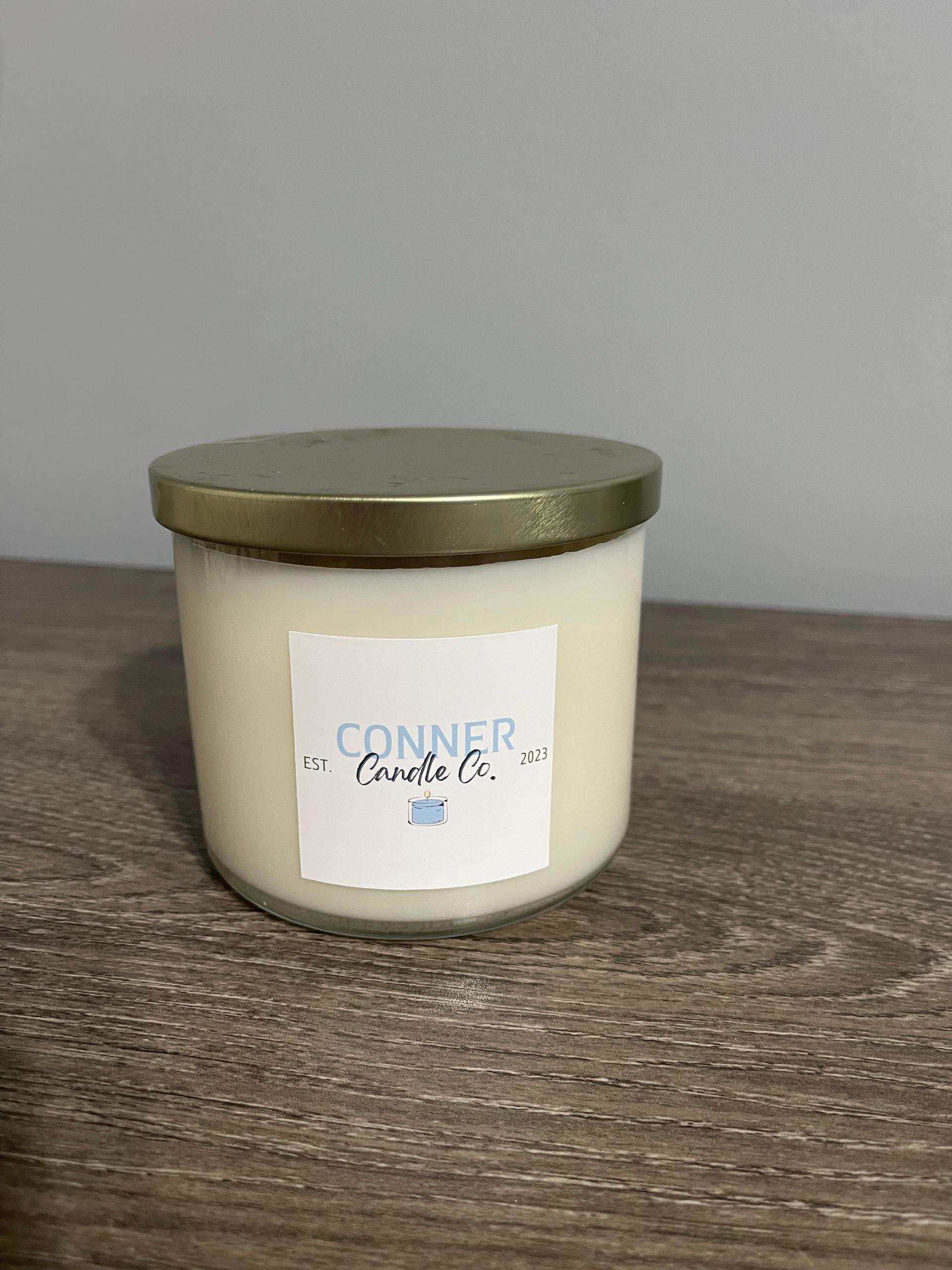 Two Conner Candle Co. candles with gold lids and white labels on a wooden surface.