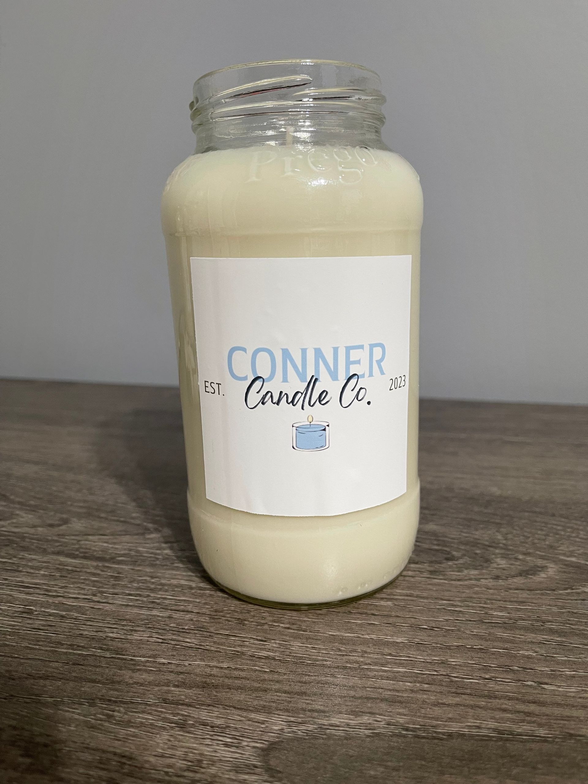 Candle in a jar with label from Conner Candle Co., on a wooden surface.