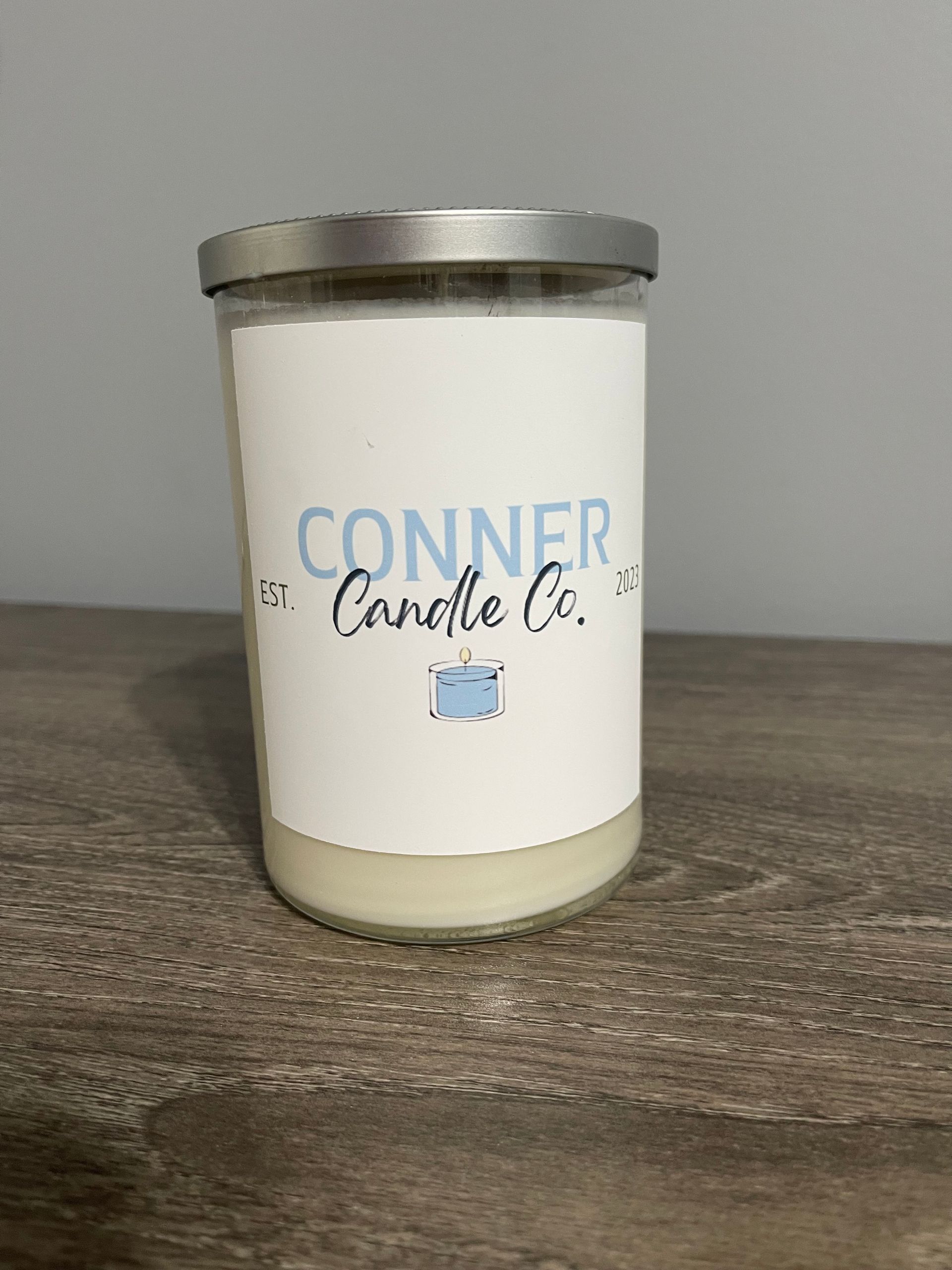 Conner Candle Co. jar candle with a silver lid and a white label, on a wooden surface.