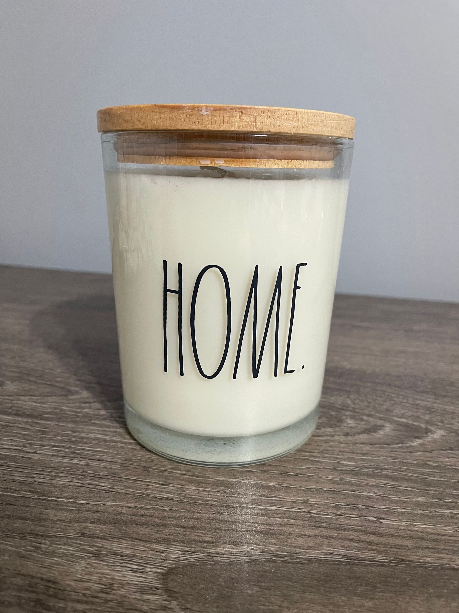 White candle in a glass jar with a wooden lid; the word 