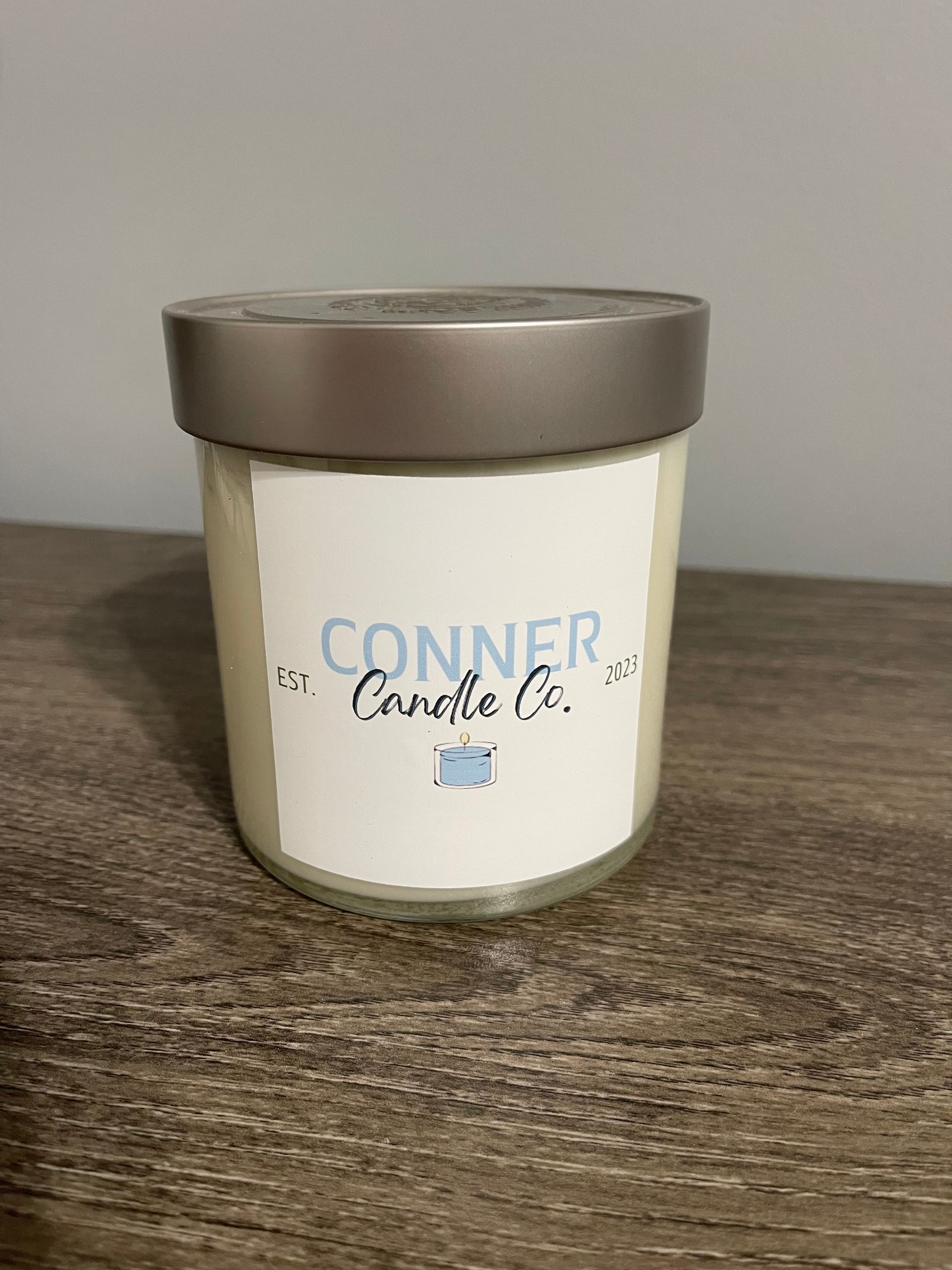 Candle in a glass jar with a silver lid, label reads 