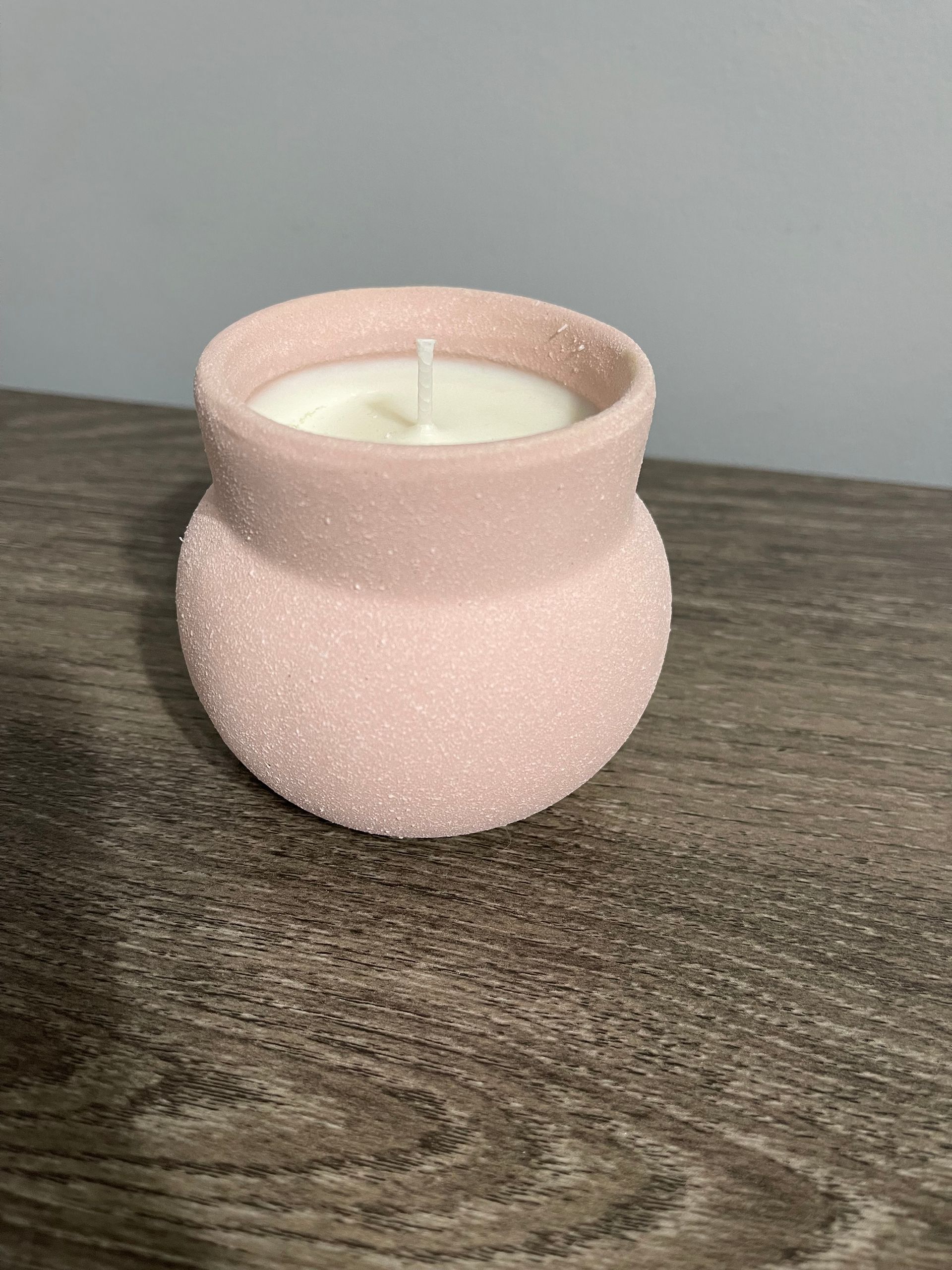 Pink candle in a textured round jar, on a wooden surface.