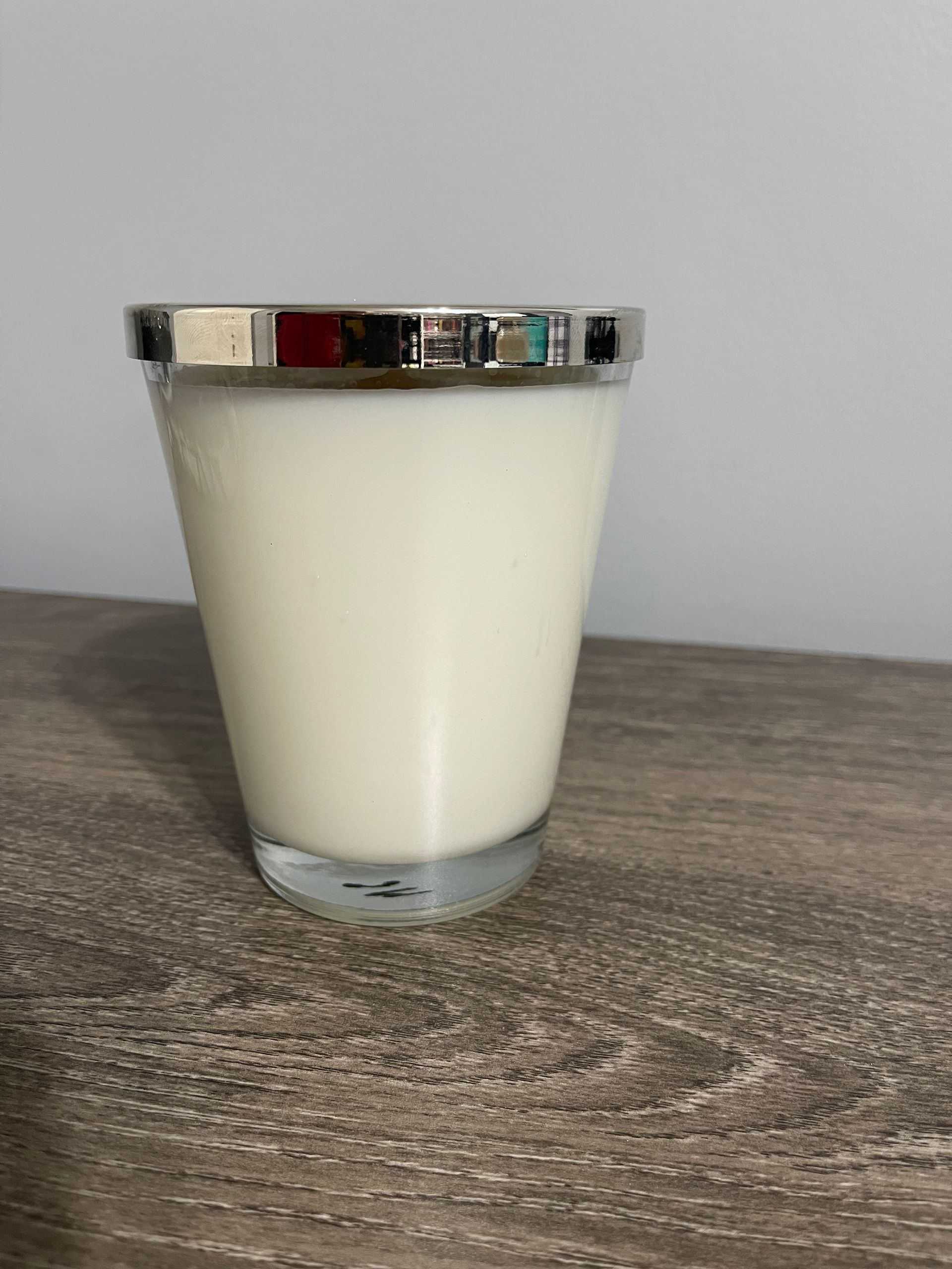 White candle in a clear glass with a silver rim, sitting on a wooden surface.
