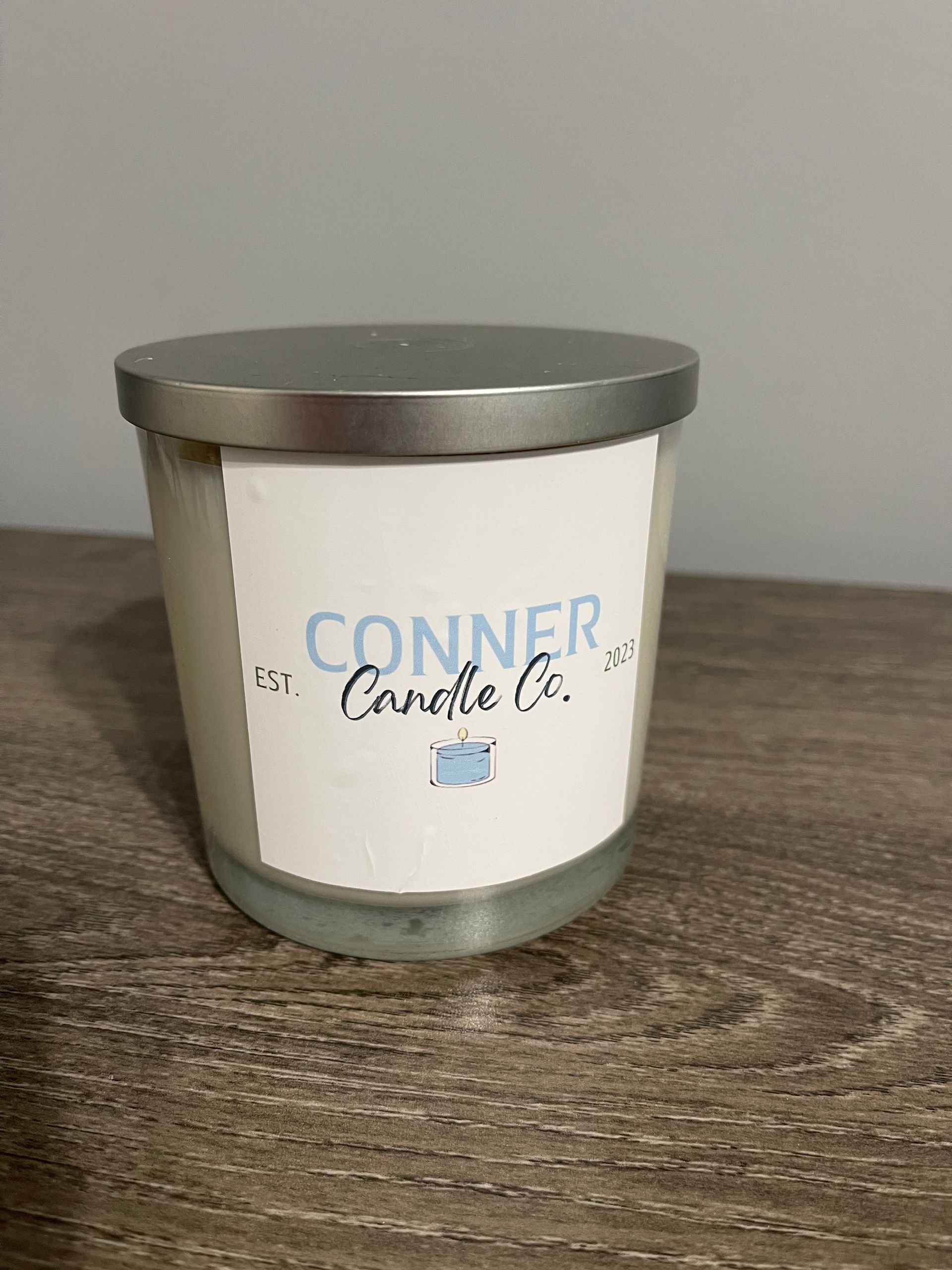 A white candle in a glass jar with a metal lid and a label that says “Conner Candle Co.”