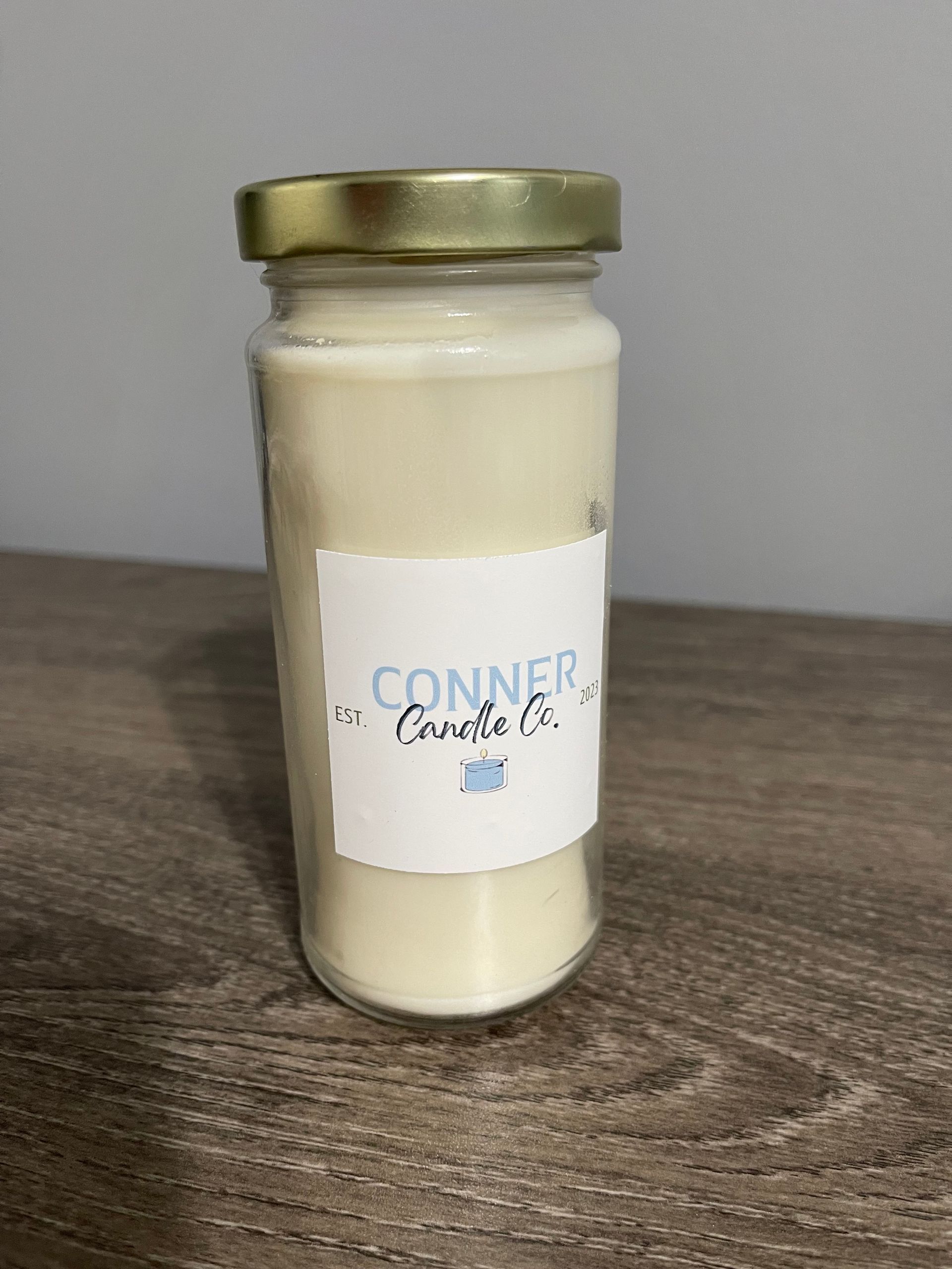 Cream-colored candle in a jar with a gold lid and a white label that reads 