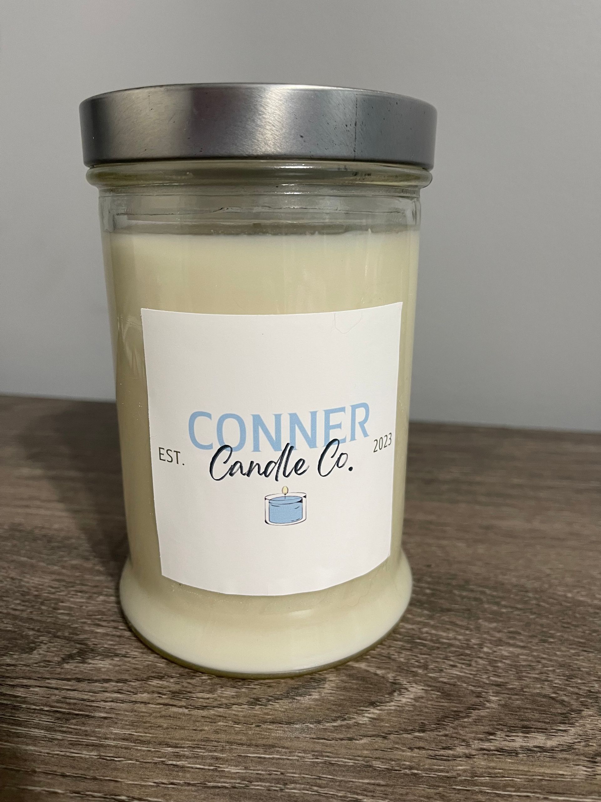 Candle in a glass jar with a silver lid. The label says Conner Candle Co. in blue on a white background.