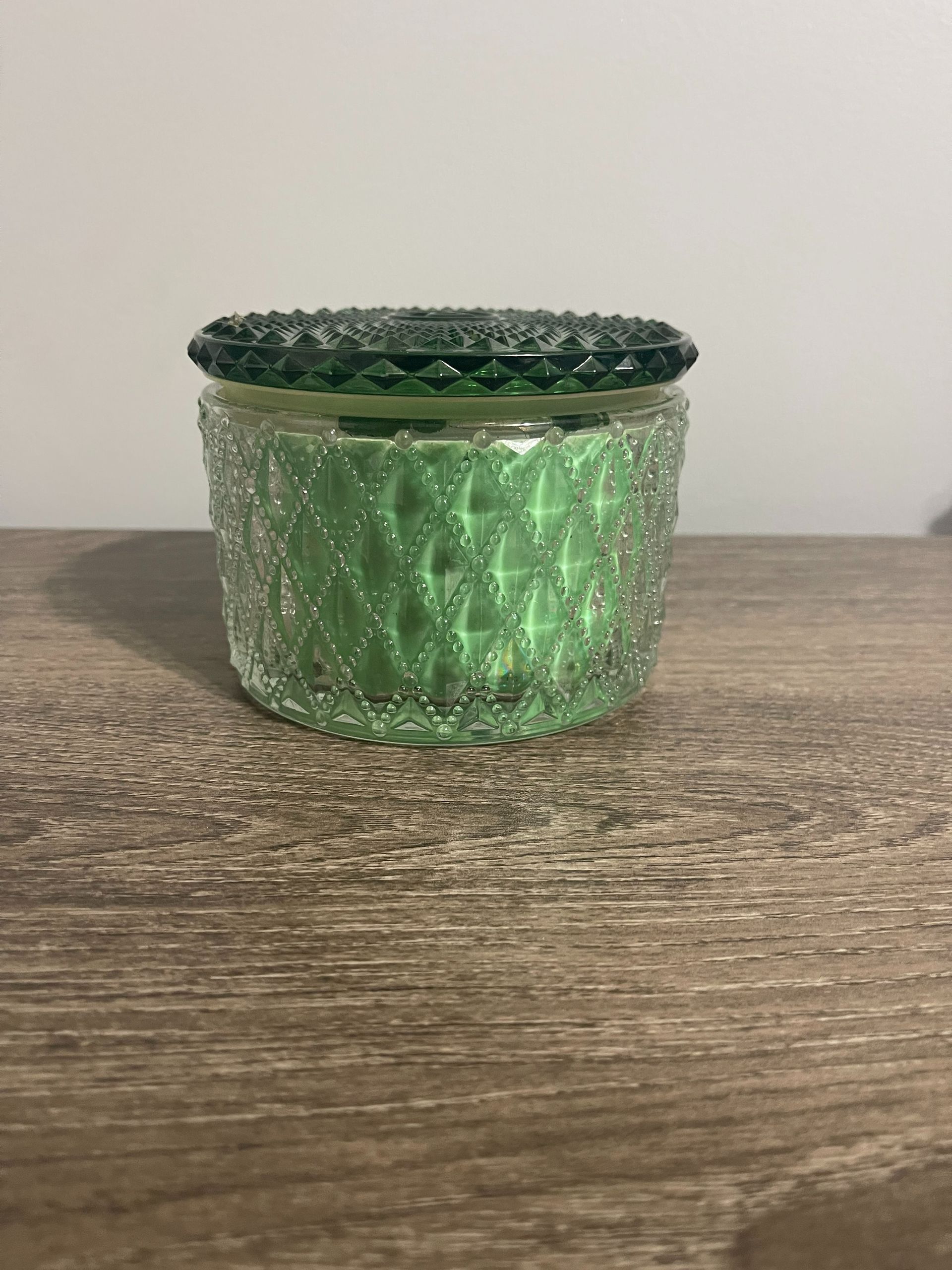 Green textured glass jar with lid on a wooden surface.