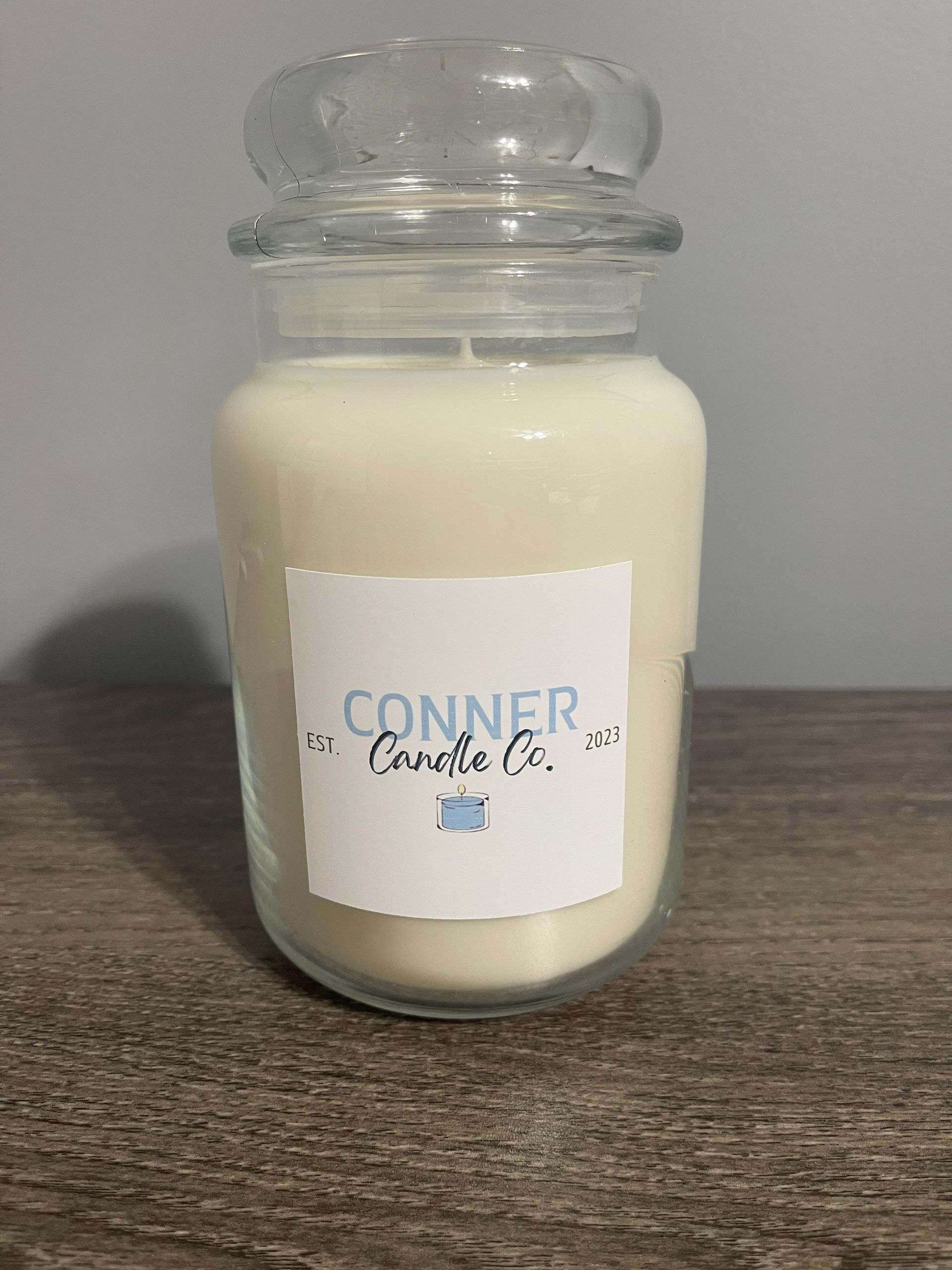 White candle in a glass jar with a clear lid, label reads 