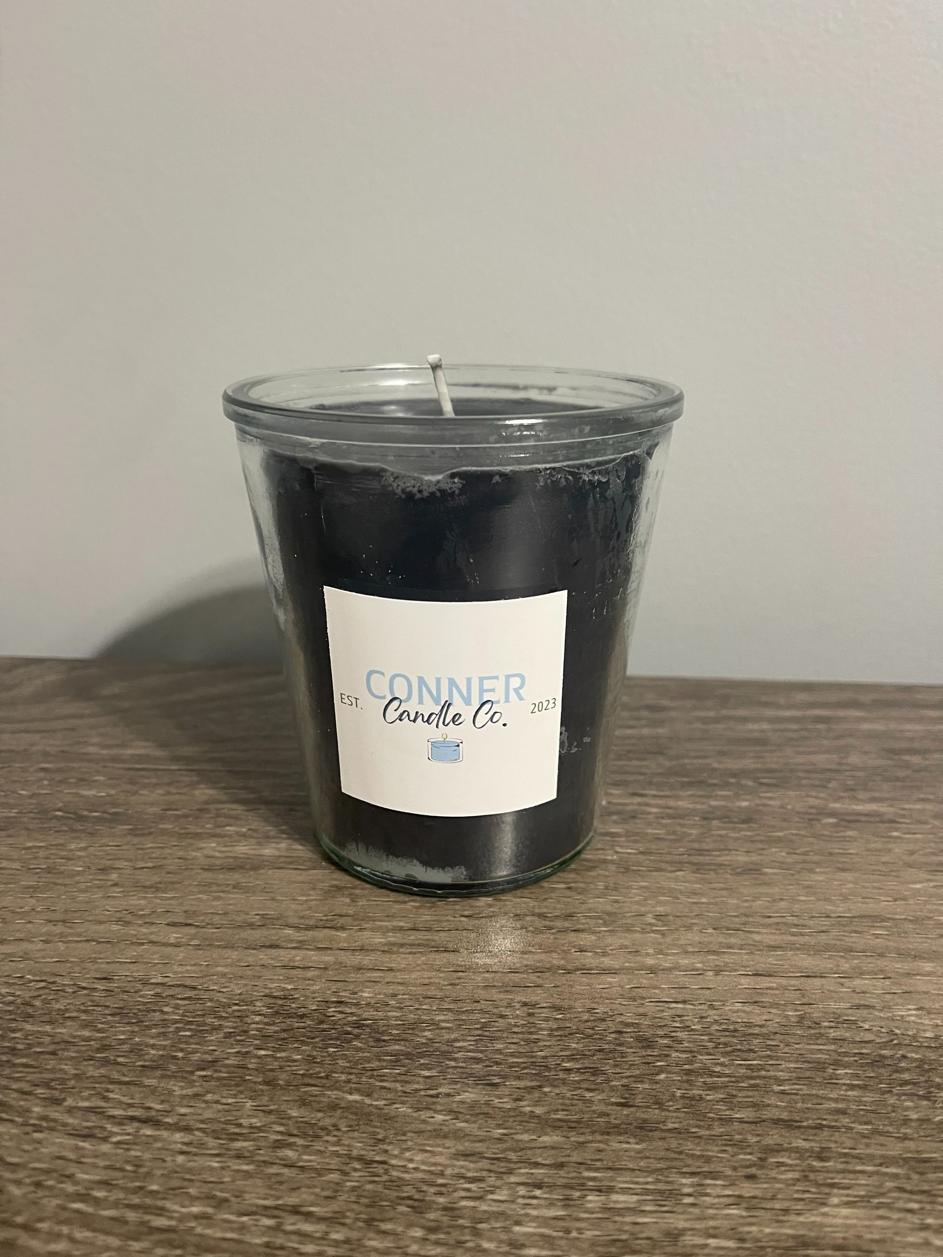 Black candle in a clear glass jar with a white label on a wooden surface.