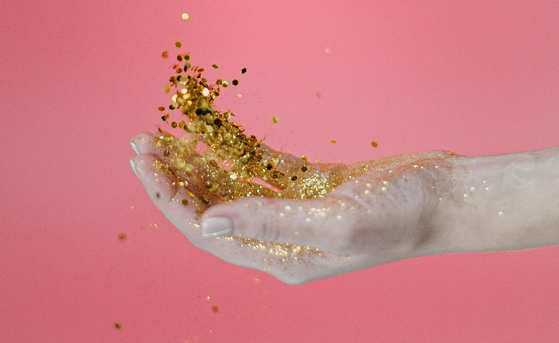 Hand catching gold glitter against a pink backdrop.