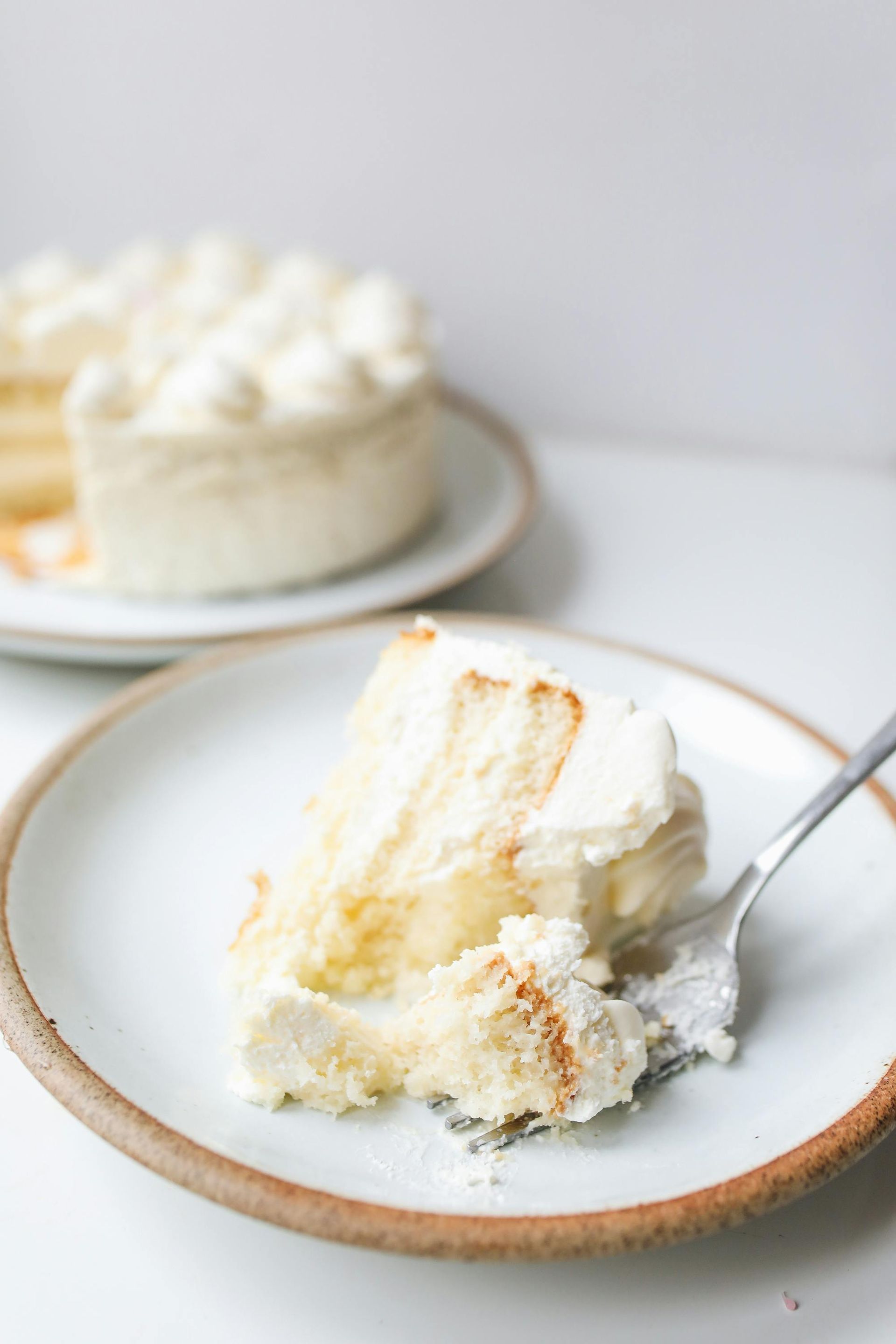 White frosted cake slice on plate with fork, whole cake in background.