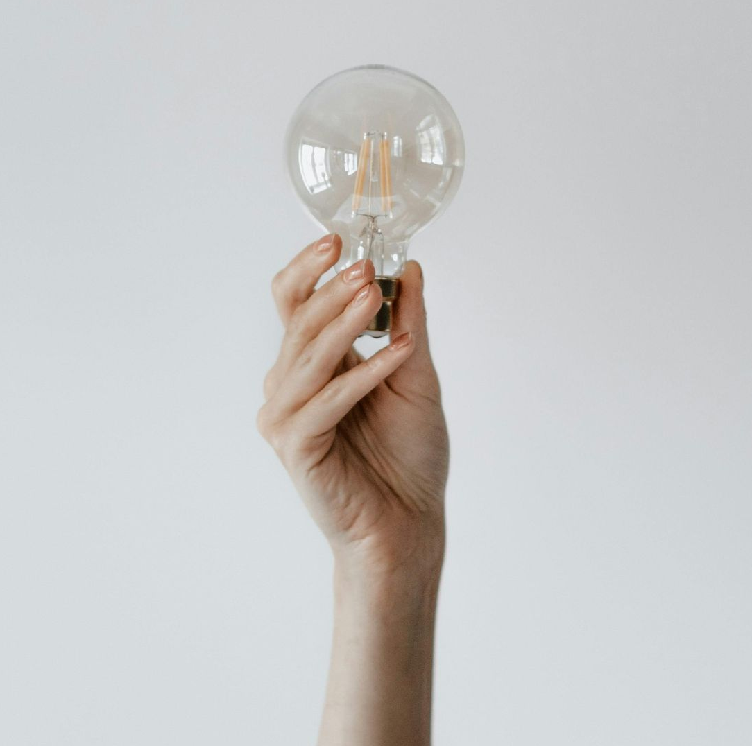 Hand holding a lit lightbulb, against a plain white background.