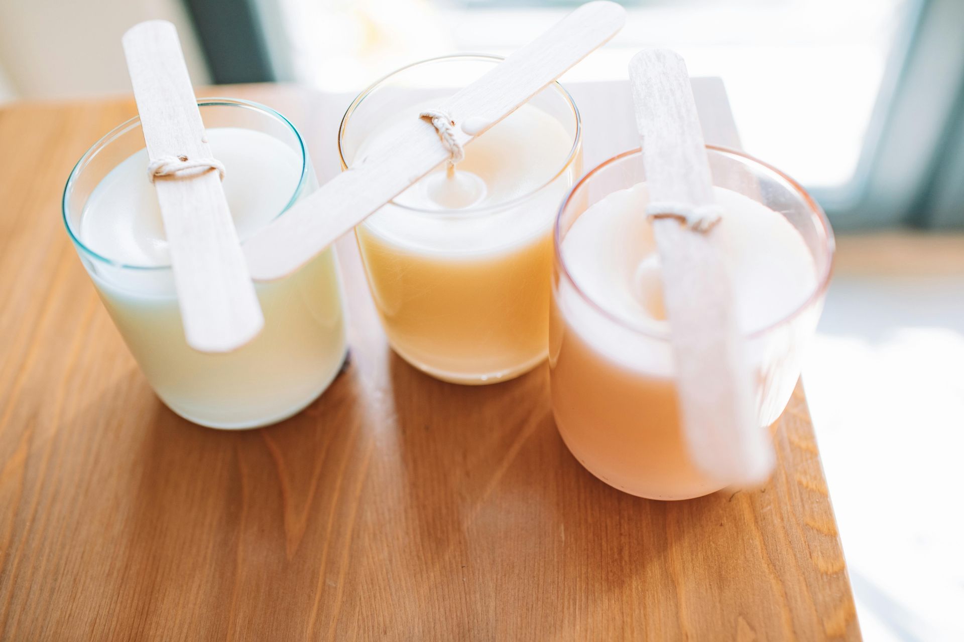 Three colored candles in glass jars with wooden sticks on a wooden surface.