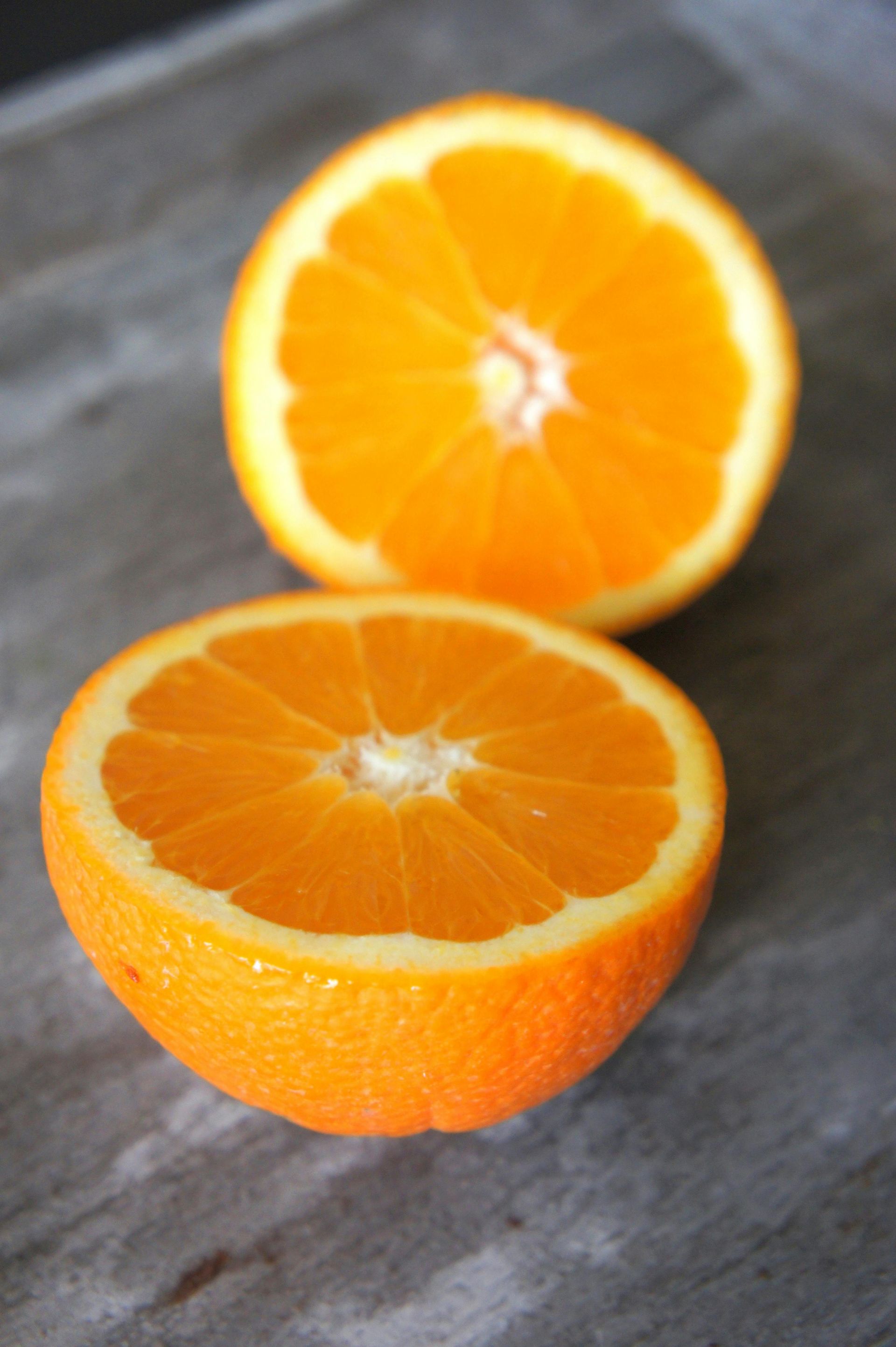 Halved orange showing juicy orange segments on a gray surface.