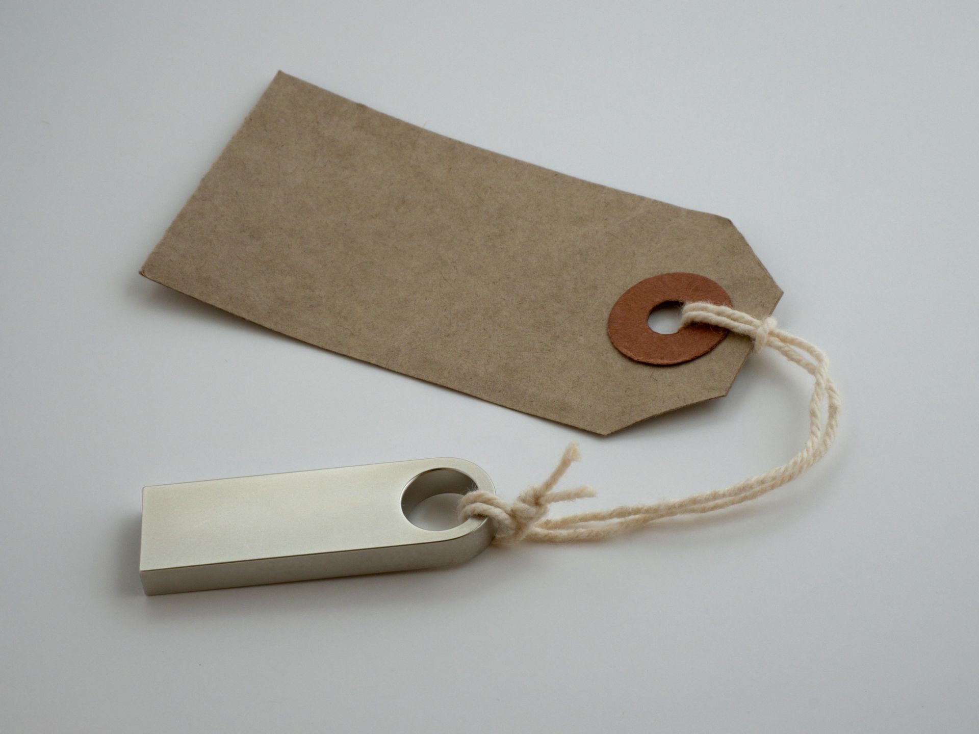 Brown paper tag tied to a silver USB drive with twine on a white surface.