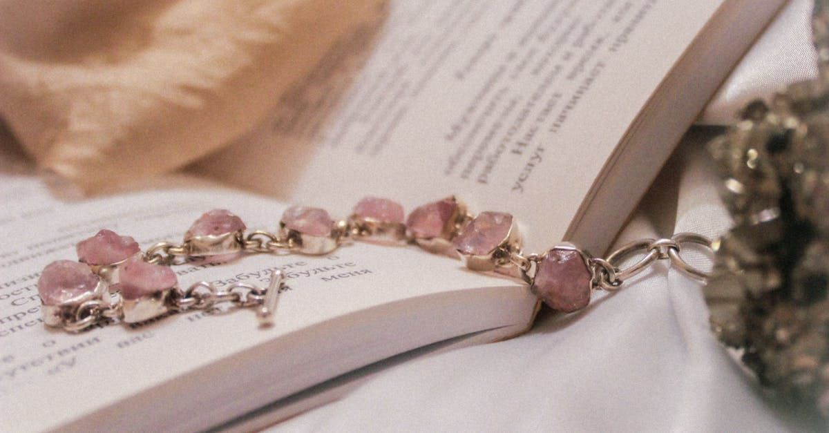Pink gemstone bracelet rests on open book with soft fabric background.