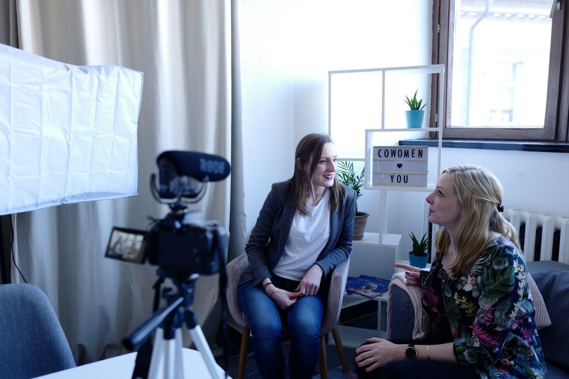 Two women seated for an interview, with a camera and softbox in a studio.
