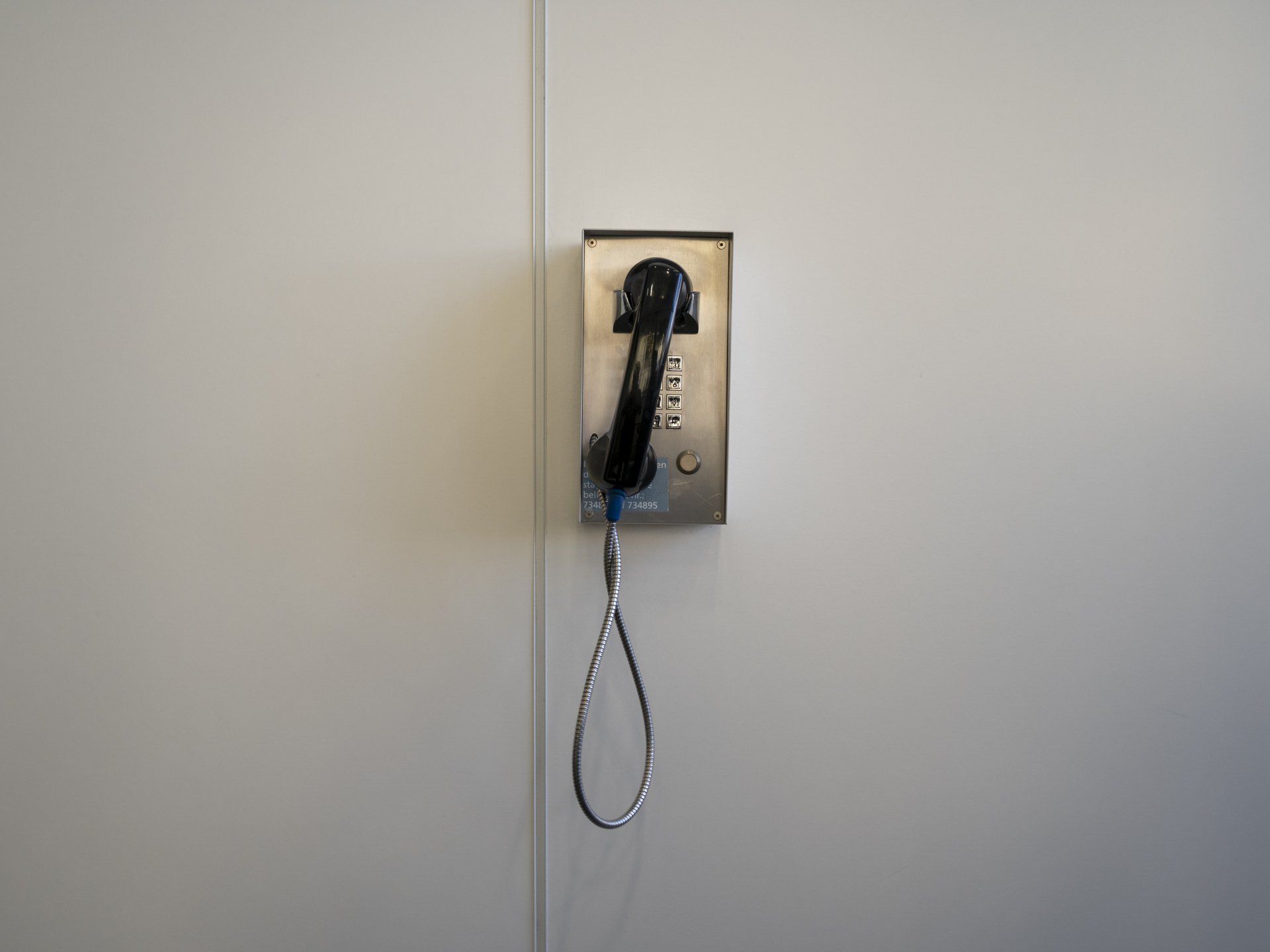 A black payphone mounted on a white wall.