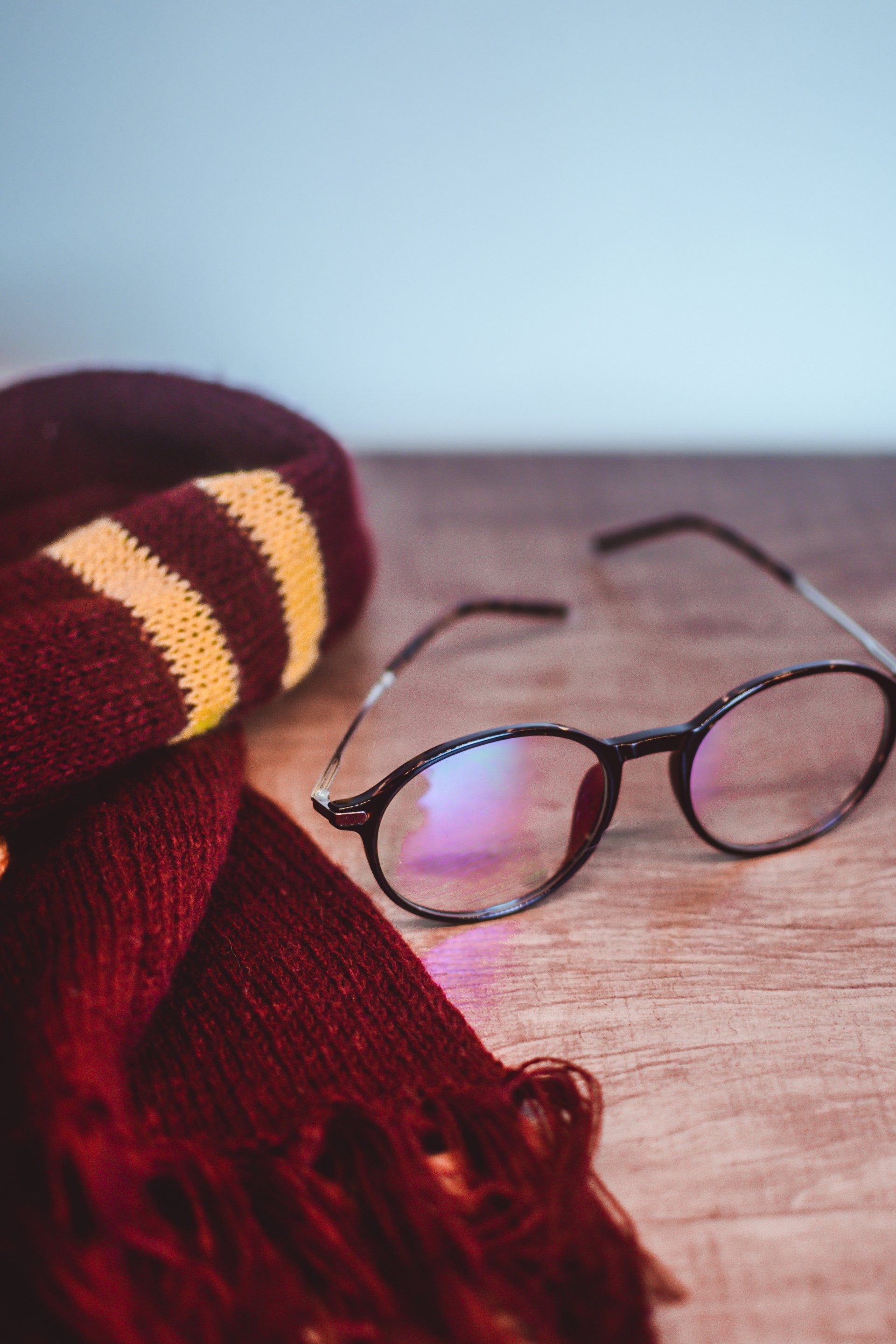 Harry Potter scarf and glasses on a wooden surface, burgundy and gold.