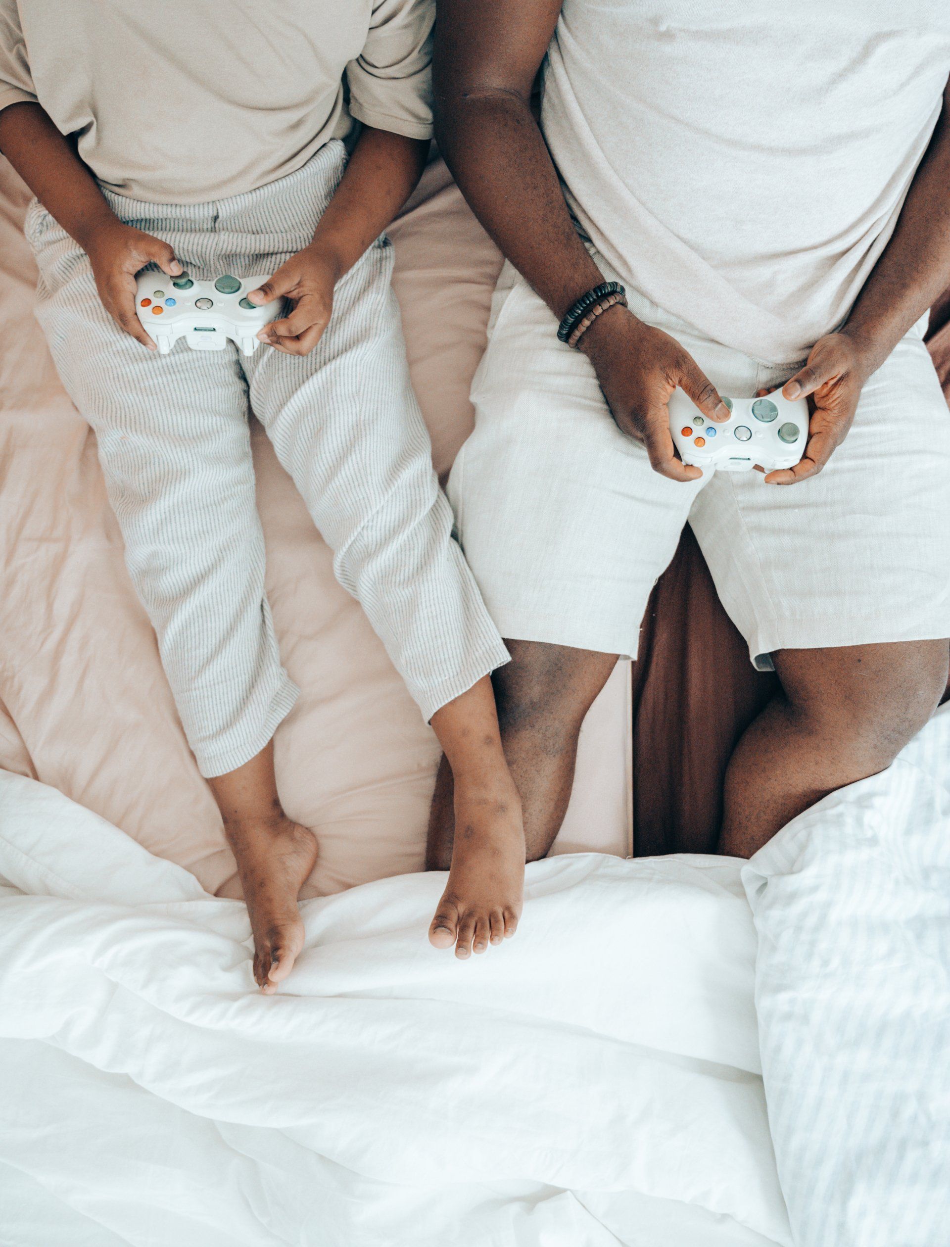 Two people in bed, holding video game controllers. Light-colored clothing and bedding.