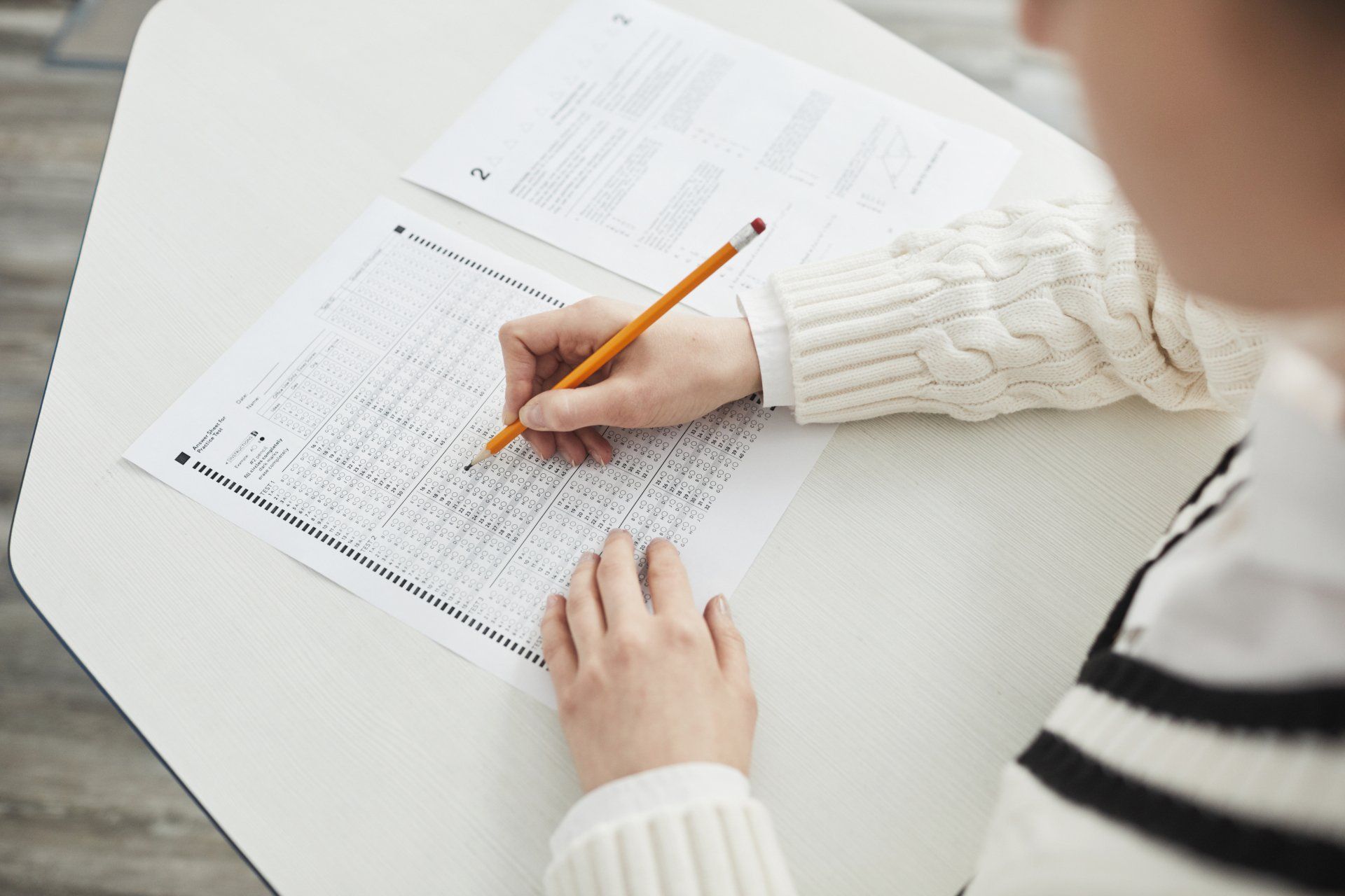 Person taking a test, filling out a form with a pencil at a white desk.