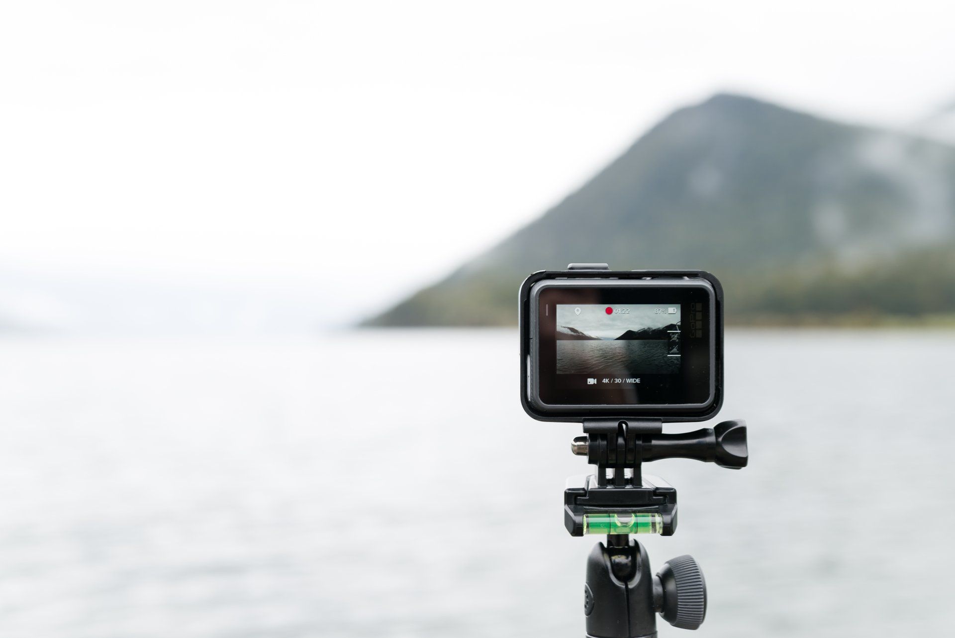 GoPro action camera on a tripod, recording a blurred lake and mountain scene.
