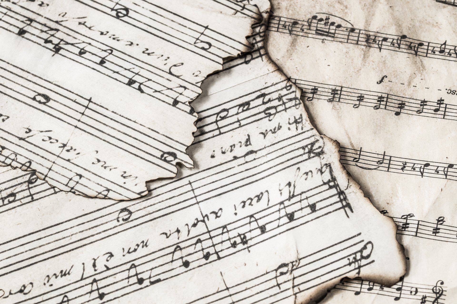 Close-up of aged sheet music with burned edges, handwritten notes and musical notation visible.