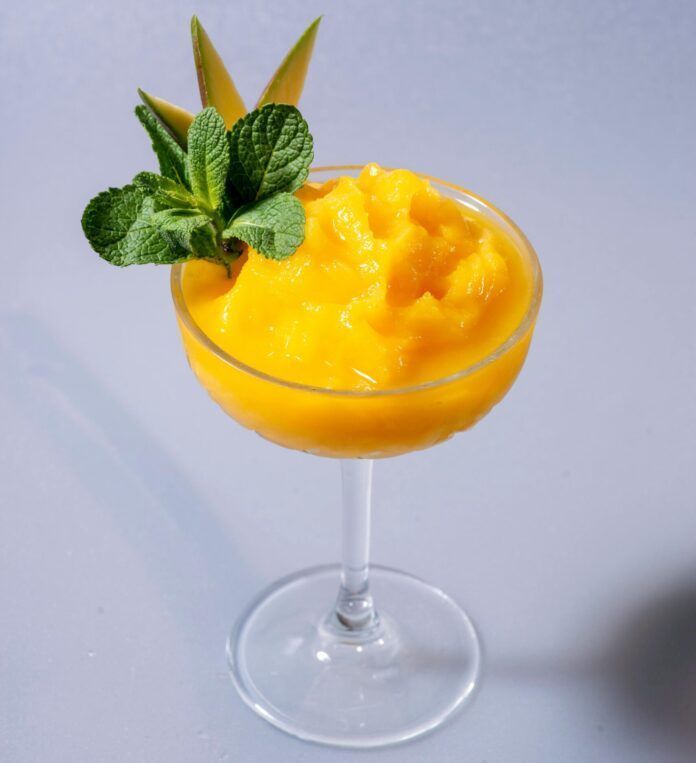 Mango smoothie in a stemmed glass, garnished with mint and mango slices.
