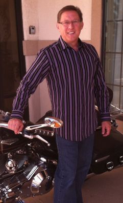 A man in a striped shirt is standing next to a motorcycle