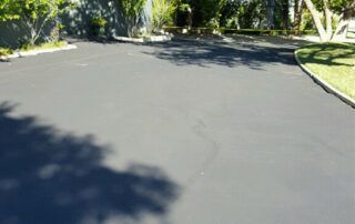 A black asphalt driveway with trees in the background.