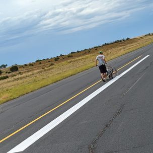 A man is pushing a wheelchair down a road