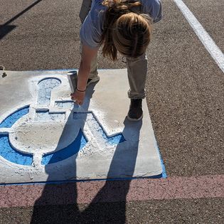 A woman is painting a handicap sign in a parking lot.