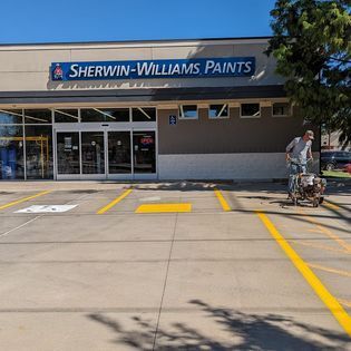 A man is painting a parking lot in front of a sherwin williams paints store