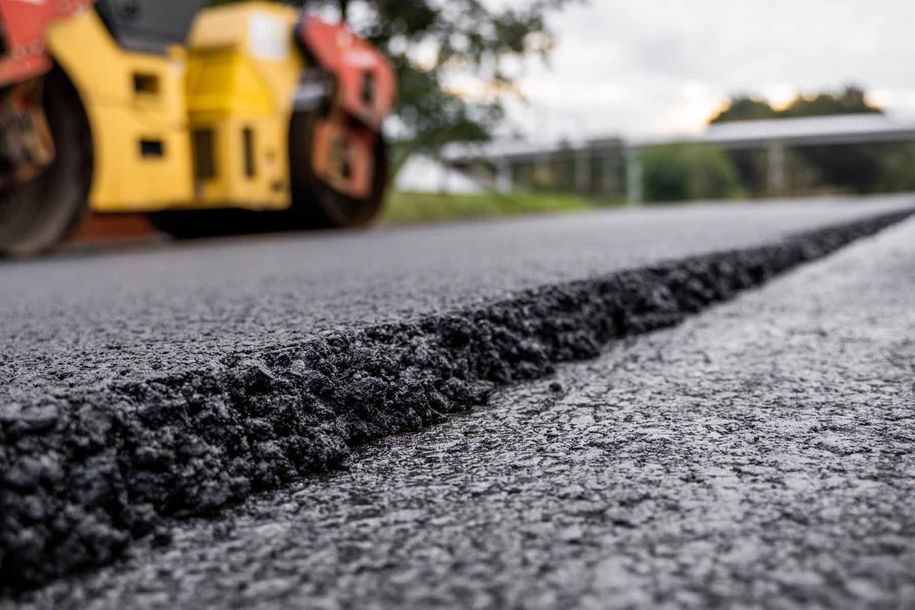 A yellow and red roller is laying asphalt on a road.