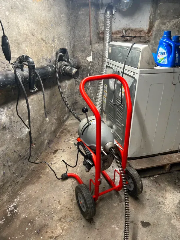 A drain cleaner is sitting next to a washer and dryer in a basement.